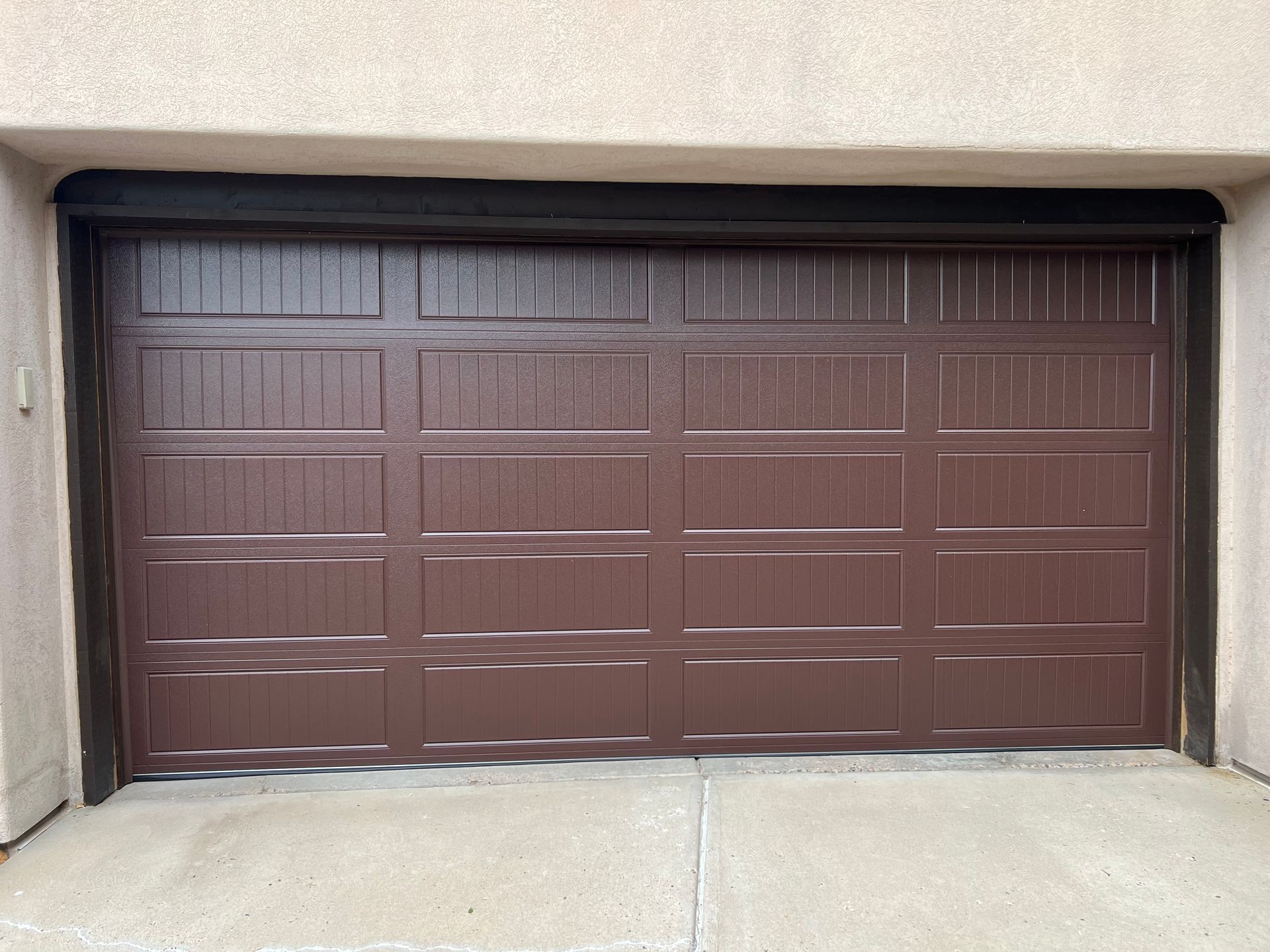 Brown closed garage door with concrete driveway, set in tan stucco exterior.