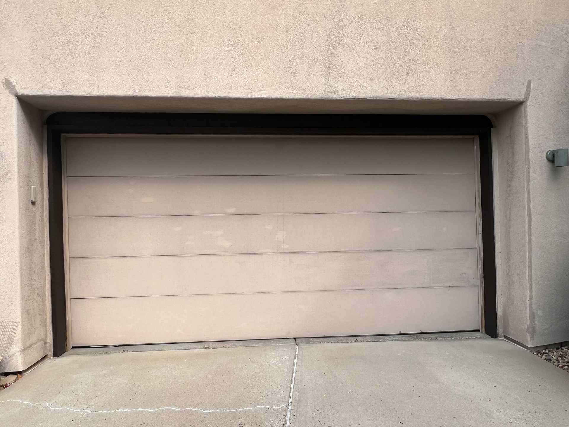 Closed beige garage door, concrete driveway, and tan stucco exterior.