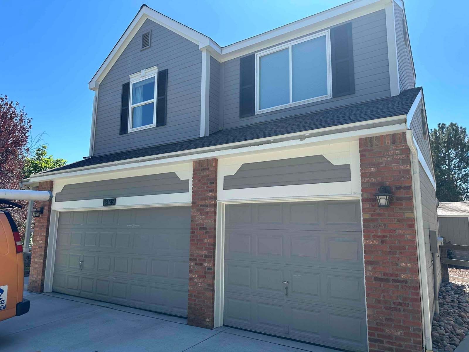 A large house with two garage doors and a truck parked in front of it.