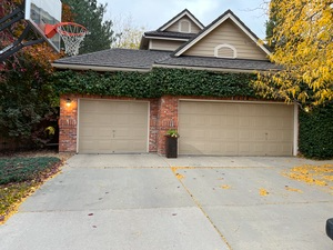 A house with two garage doors and a basketball hoop in front of it.