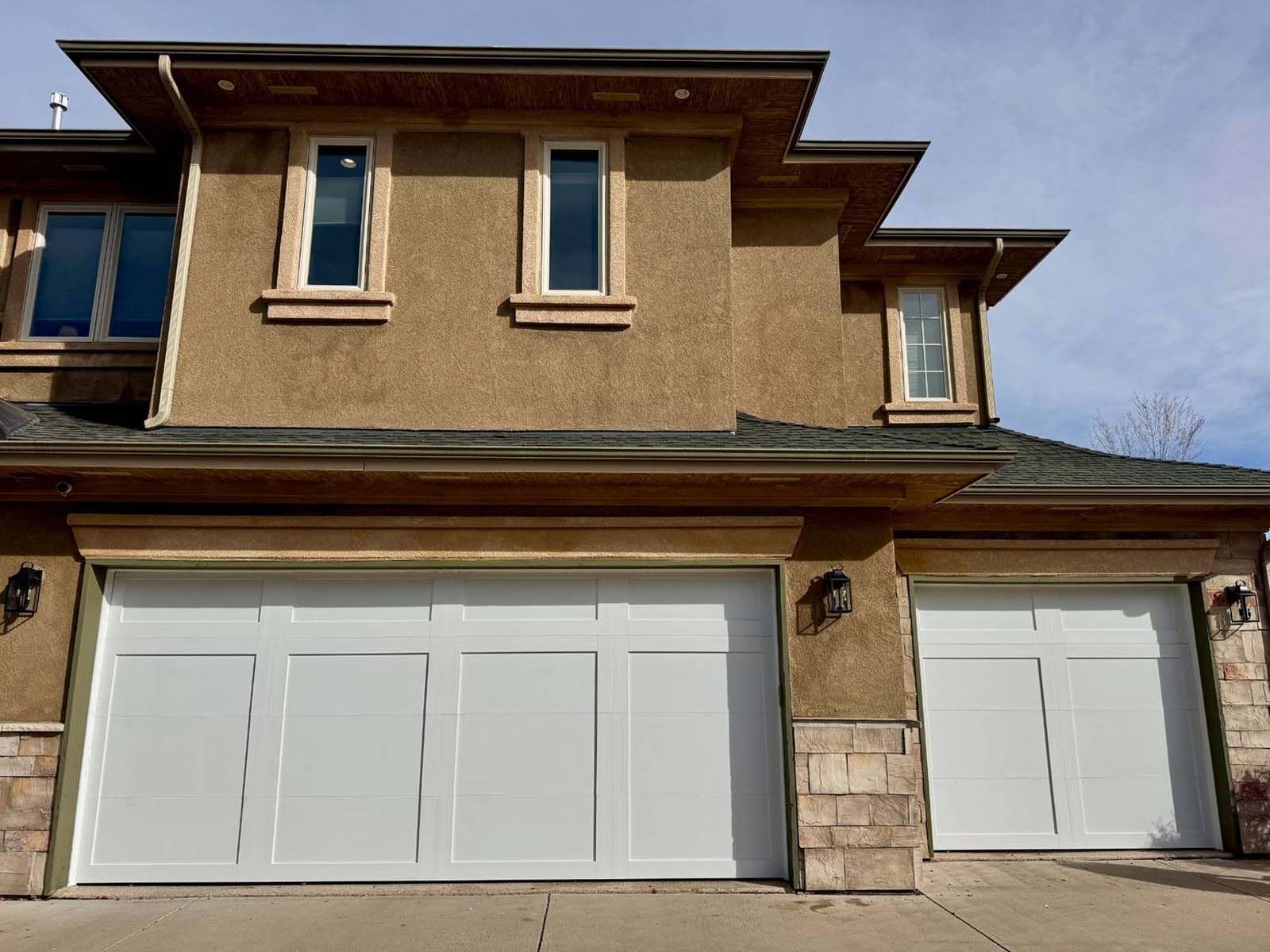 A large house with two white garage doors and three windows.