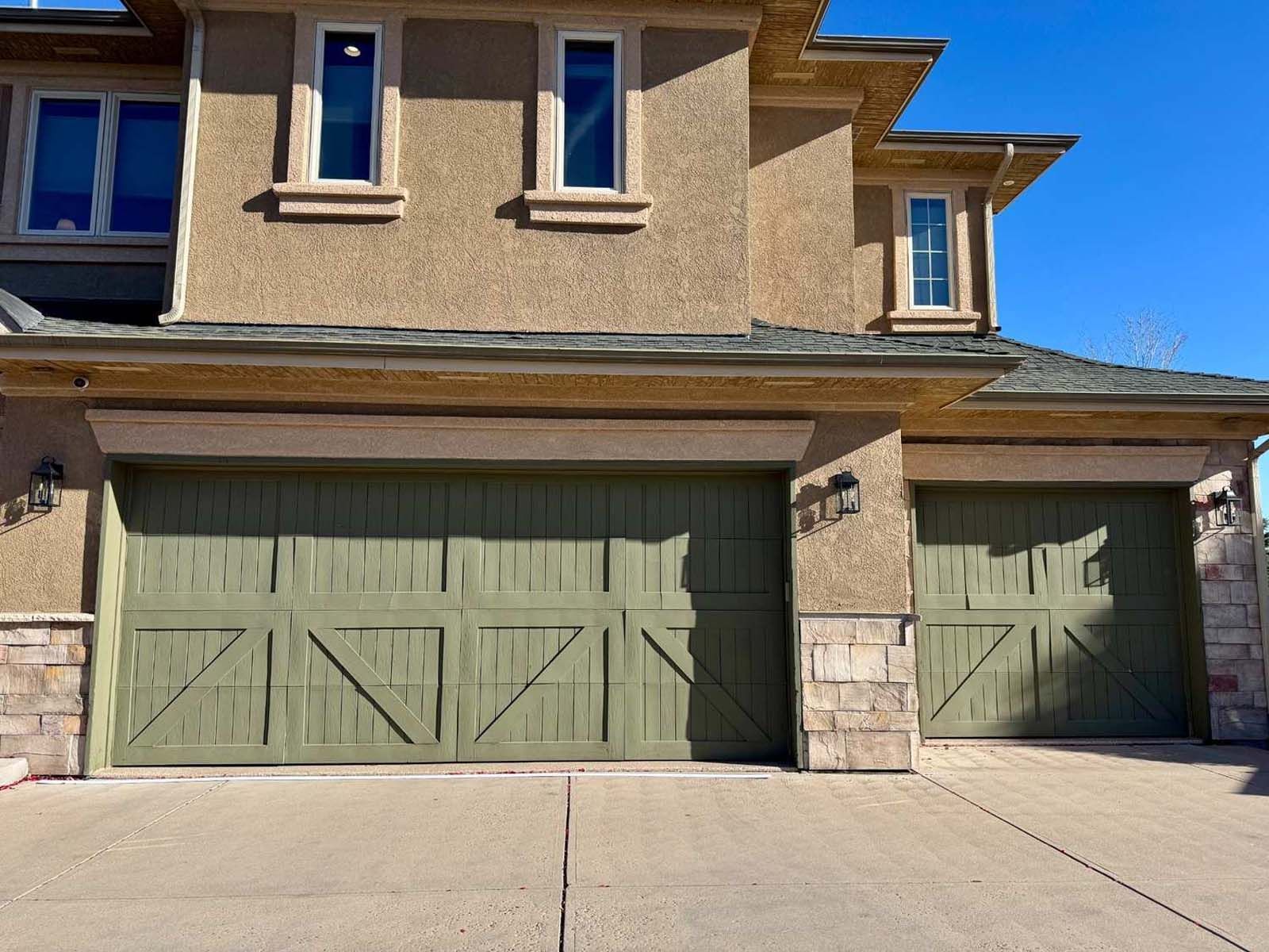 A large house with two green garage doors and a concrete driveway.