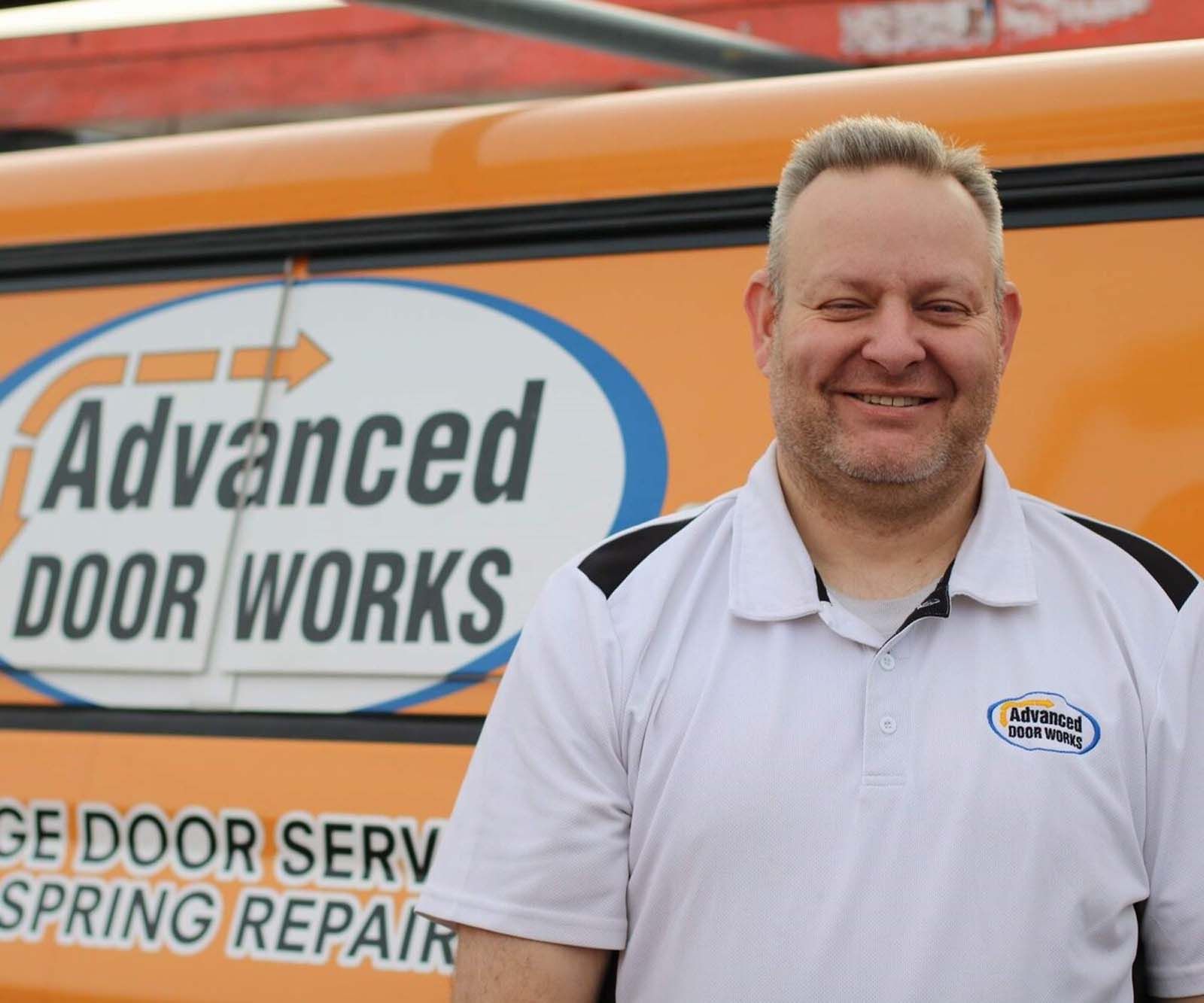 A man standing in front of an orange van that says advanced door works