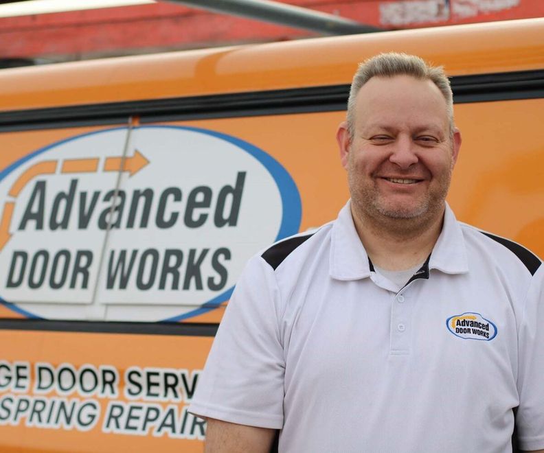 A man standing in front of an orange van that says advanced door works