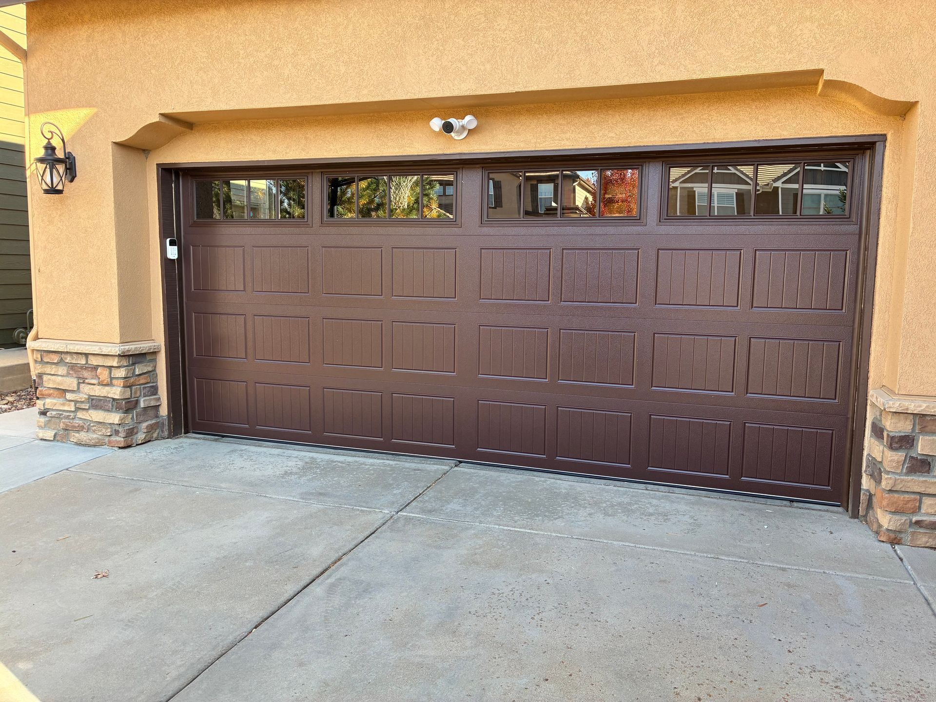 Brown garage door with windows, on a house with stone accents, concrete driveway.