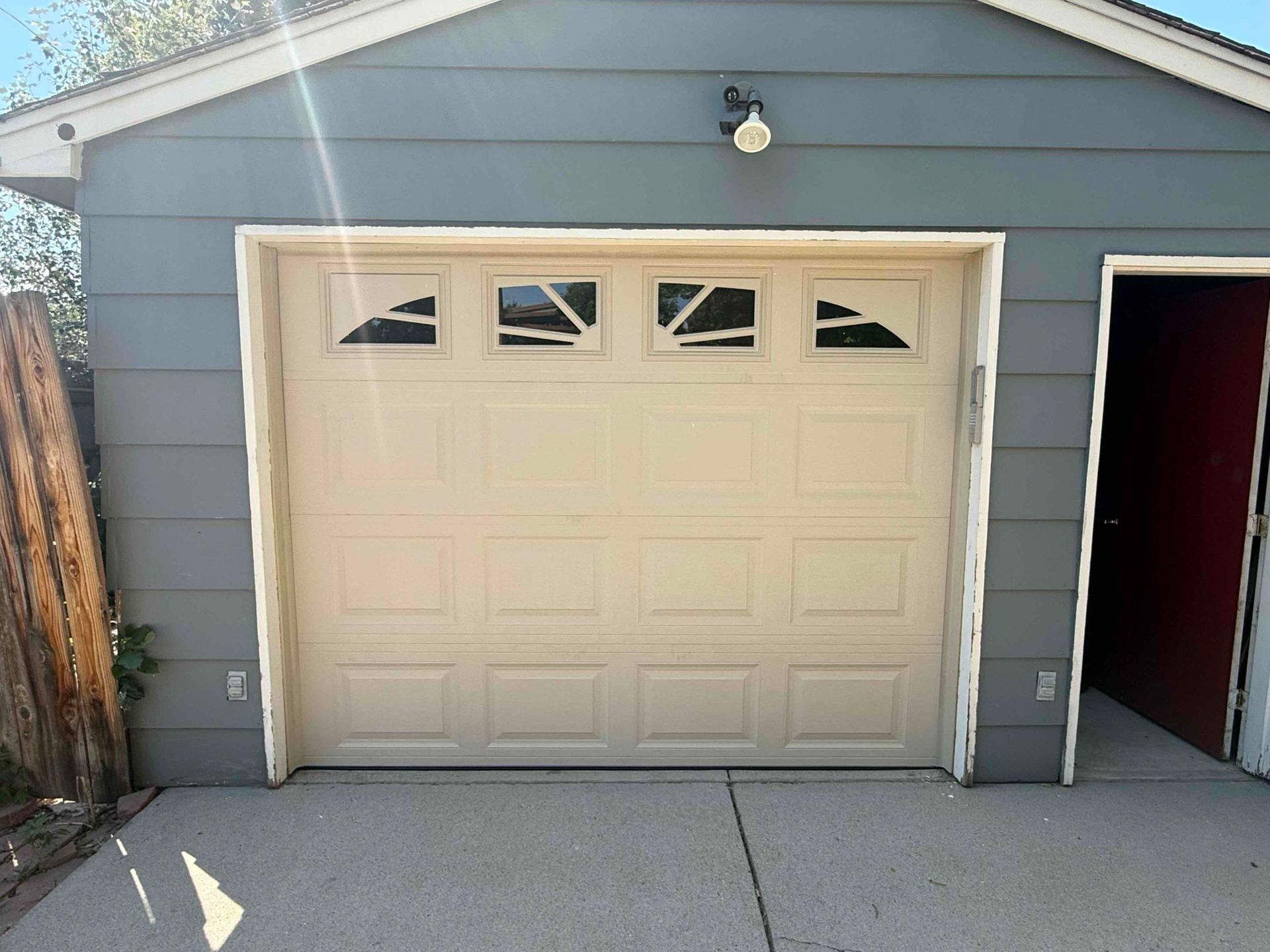 Tan garage door with windows, on a blue-gray building, next to an open red door.