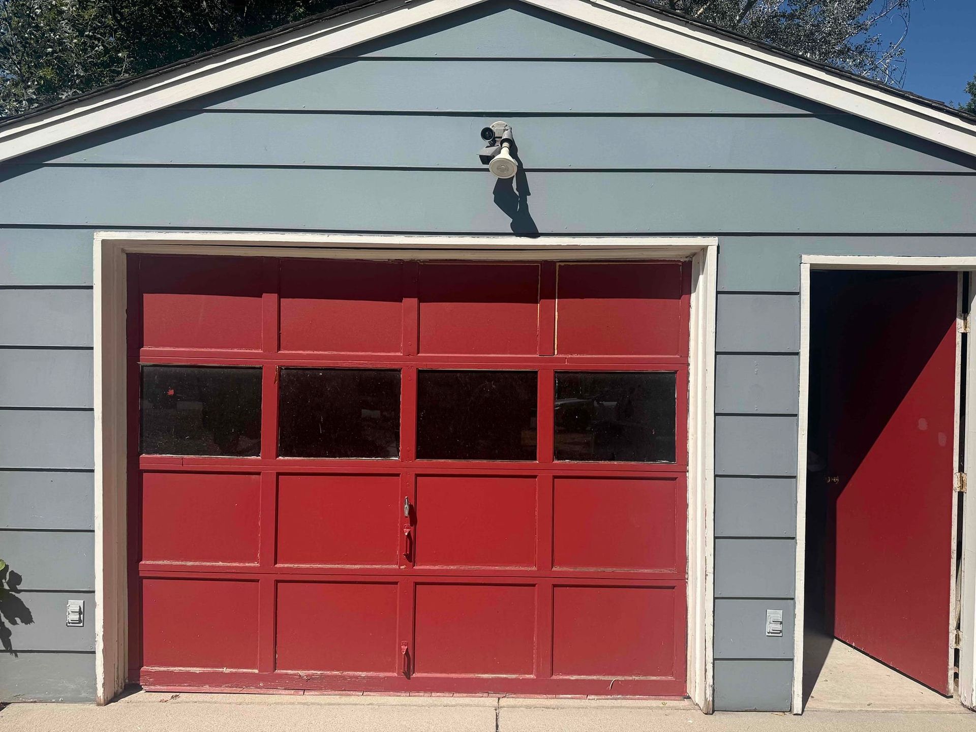 Red garage door with windows, next to an open red door. Blue siding and white trim.
