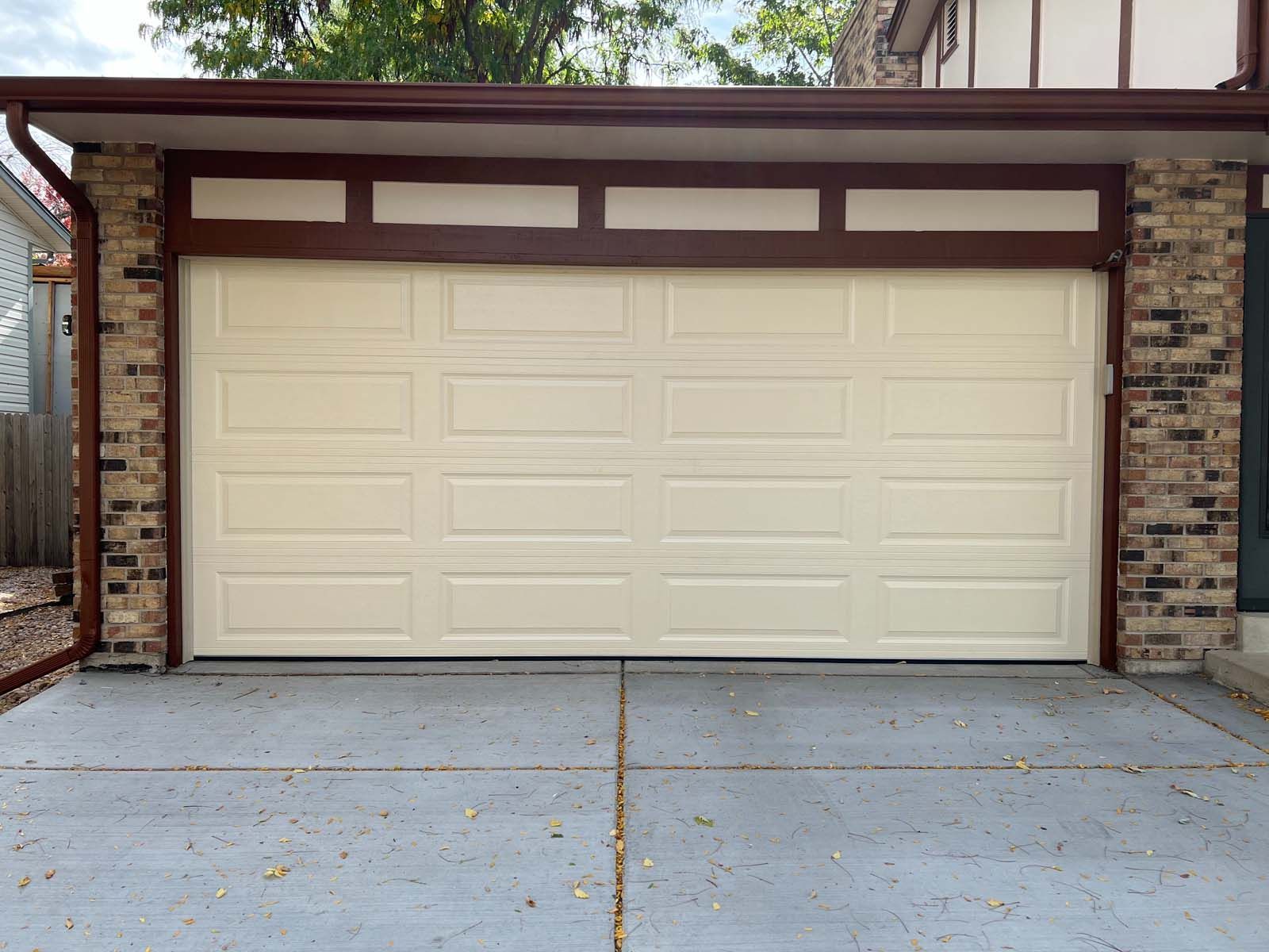 A white garage door is sitting in front of a brick house.