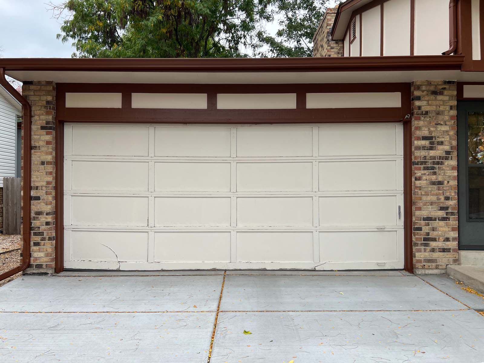 A white garage door is sitting in front of a brick house.