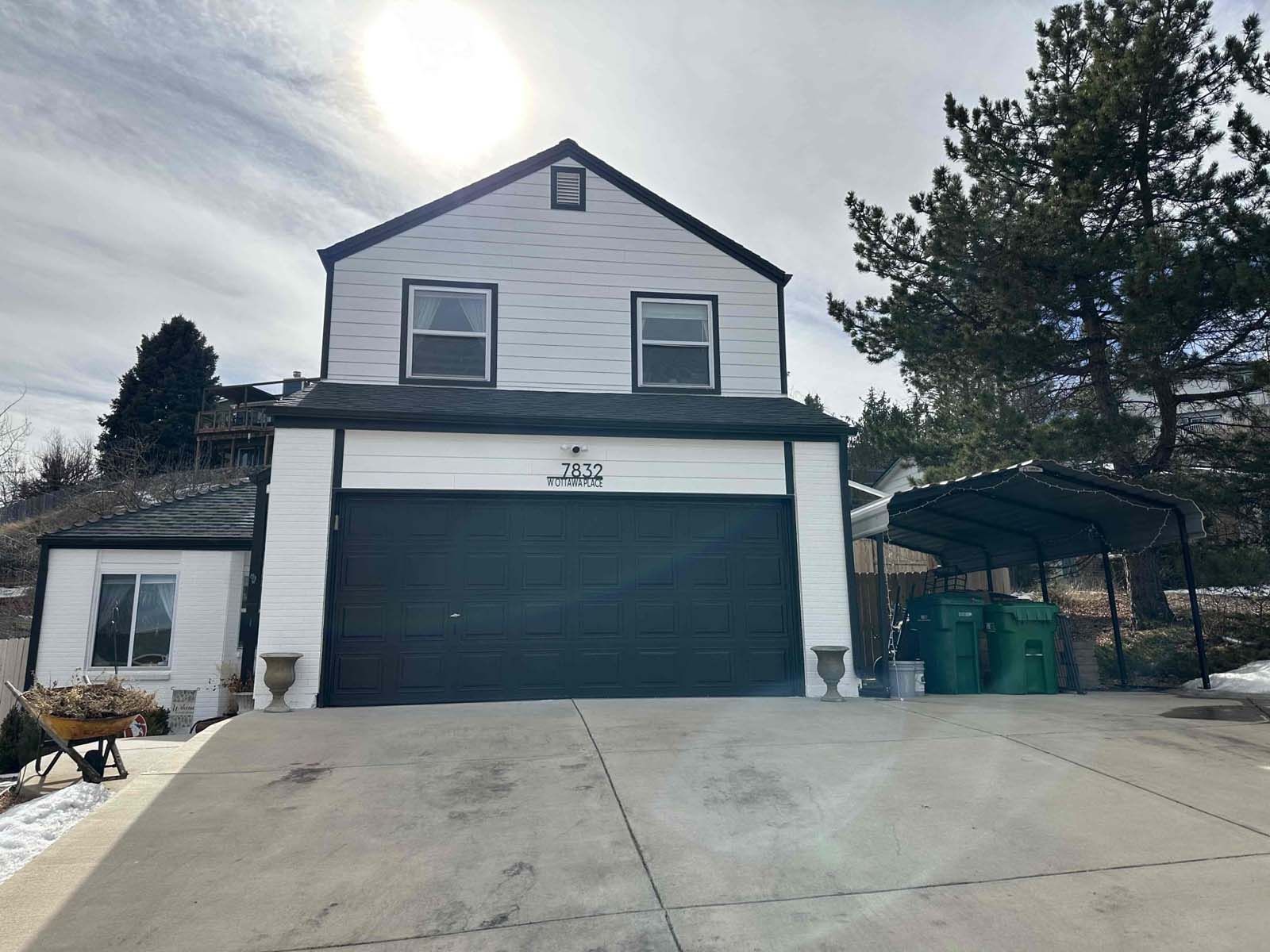 A white house with a black garage door and a carport.