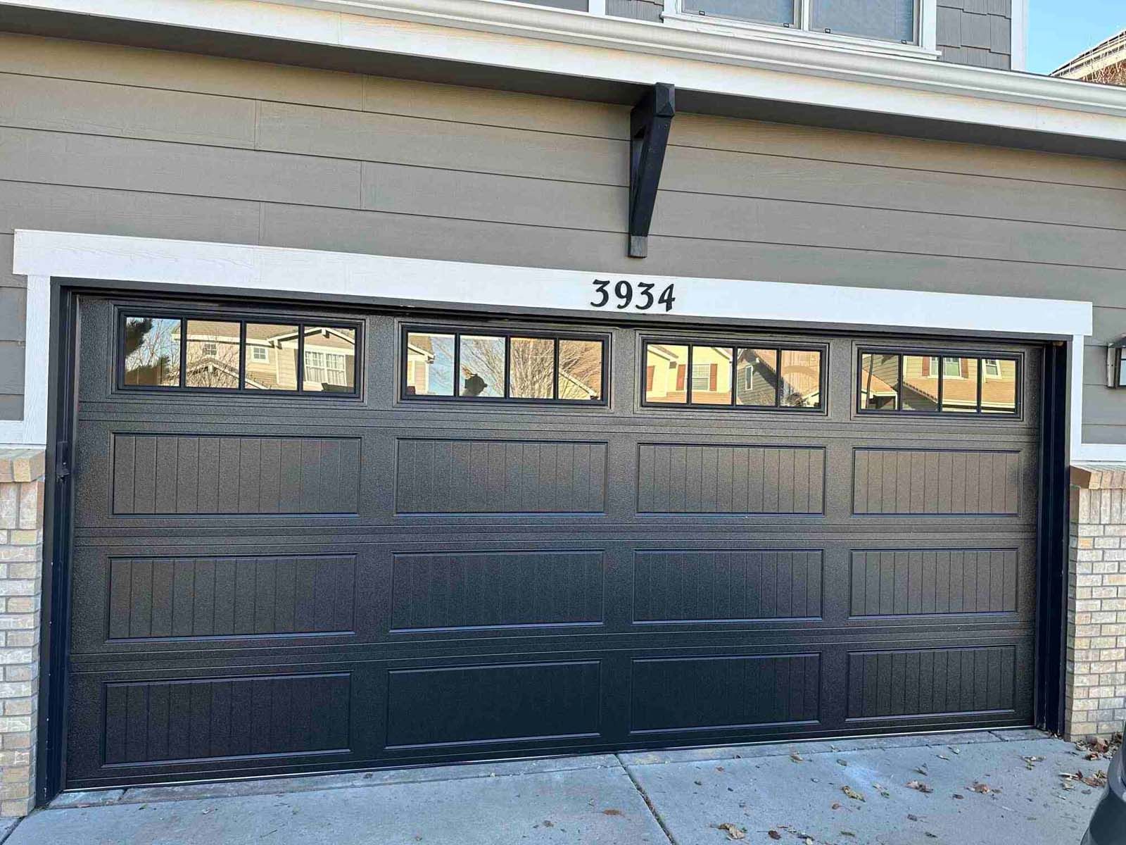 A black garage door is sitting in front of a house.
