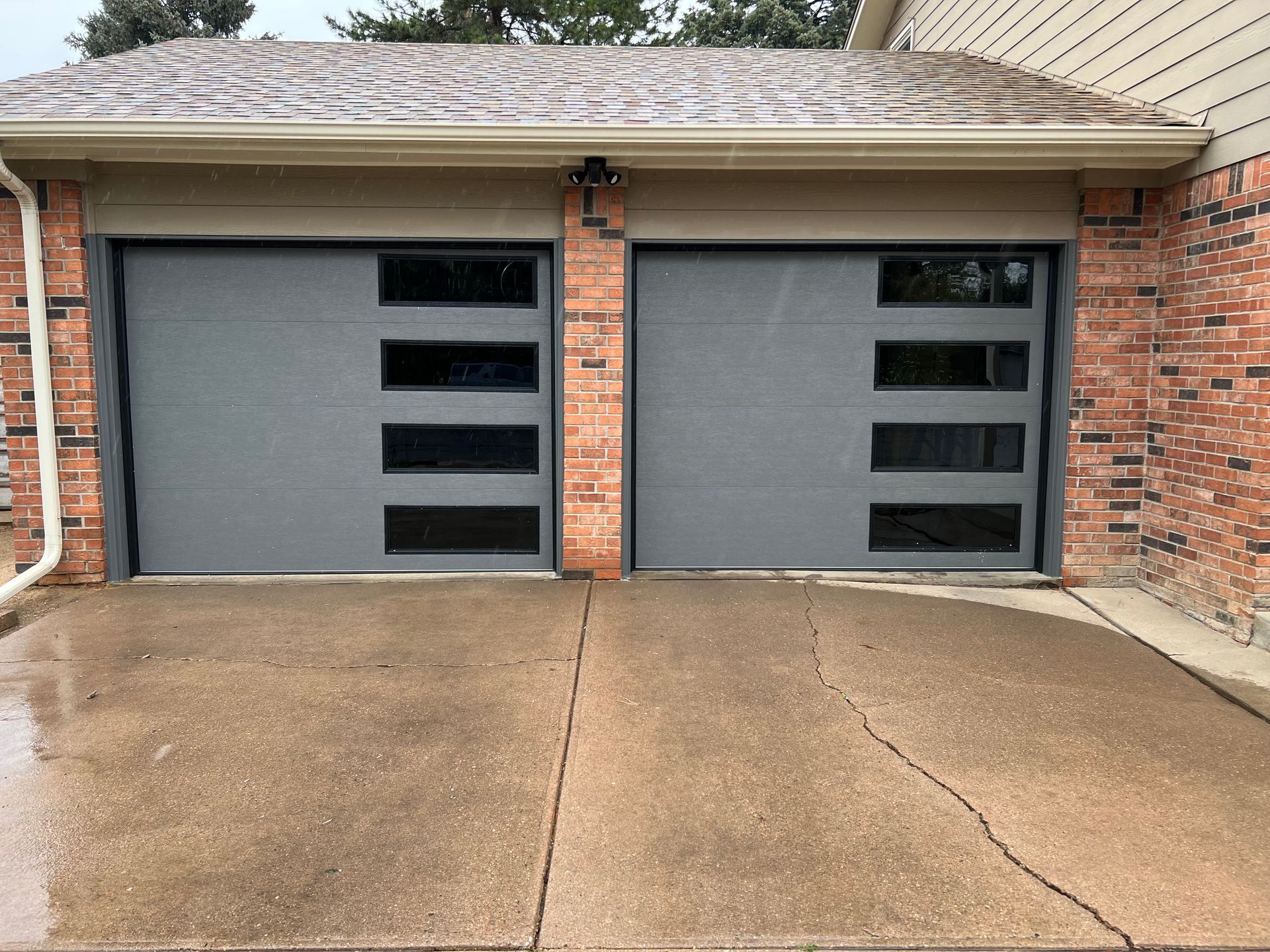 A brick house with two garage doors and a concrete driveway.