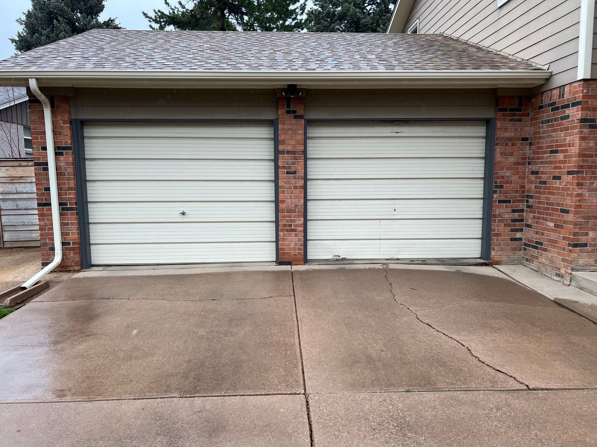 A brick house with two garage doors and a concrete driveway