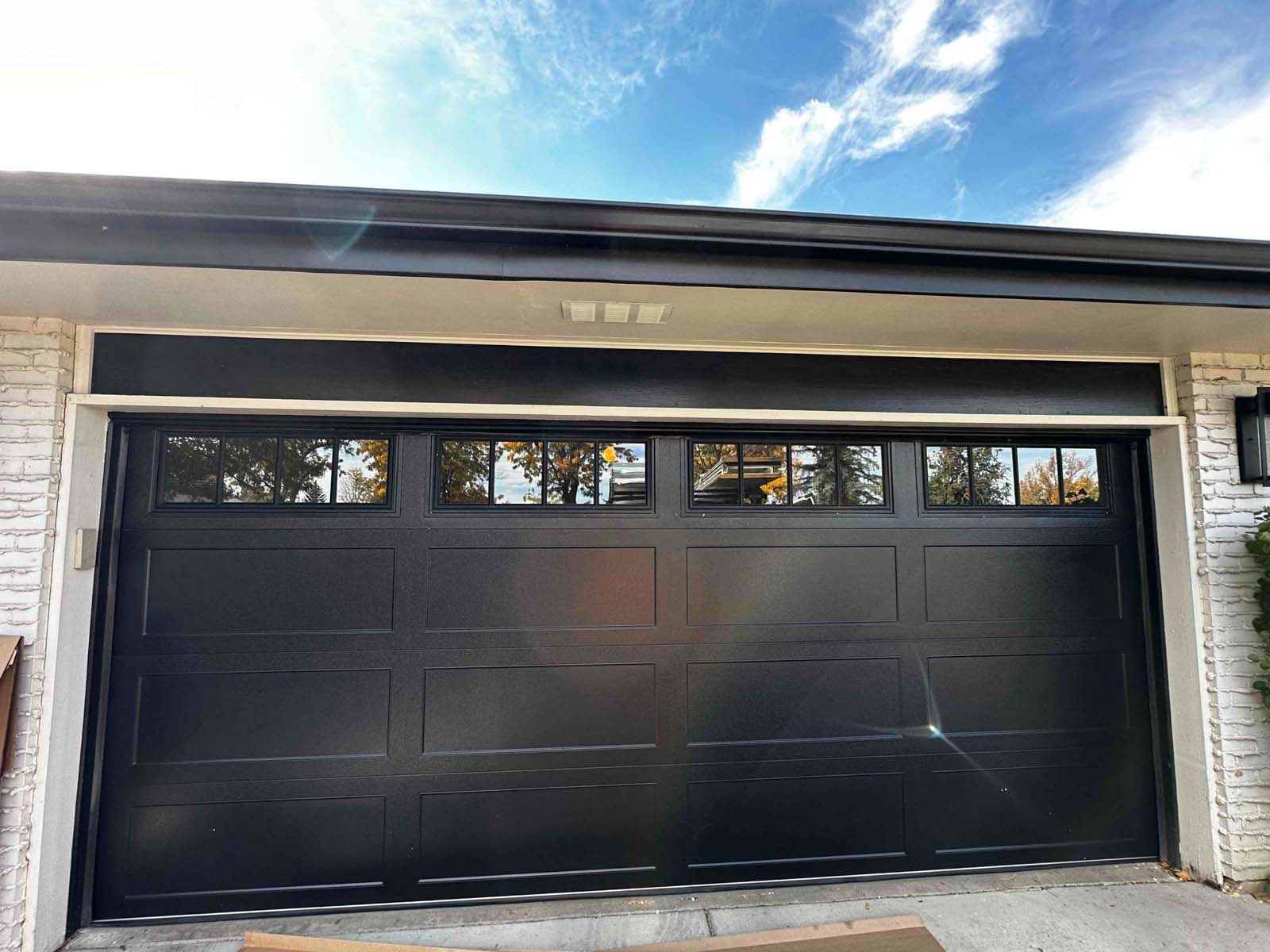 A black garage door is sitting in front of a white brick house.