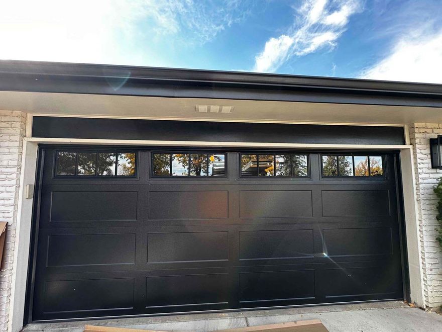 A black garage door is sitting in front of a white brick house.