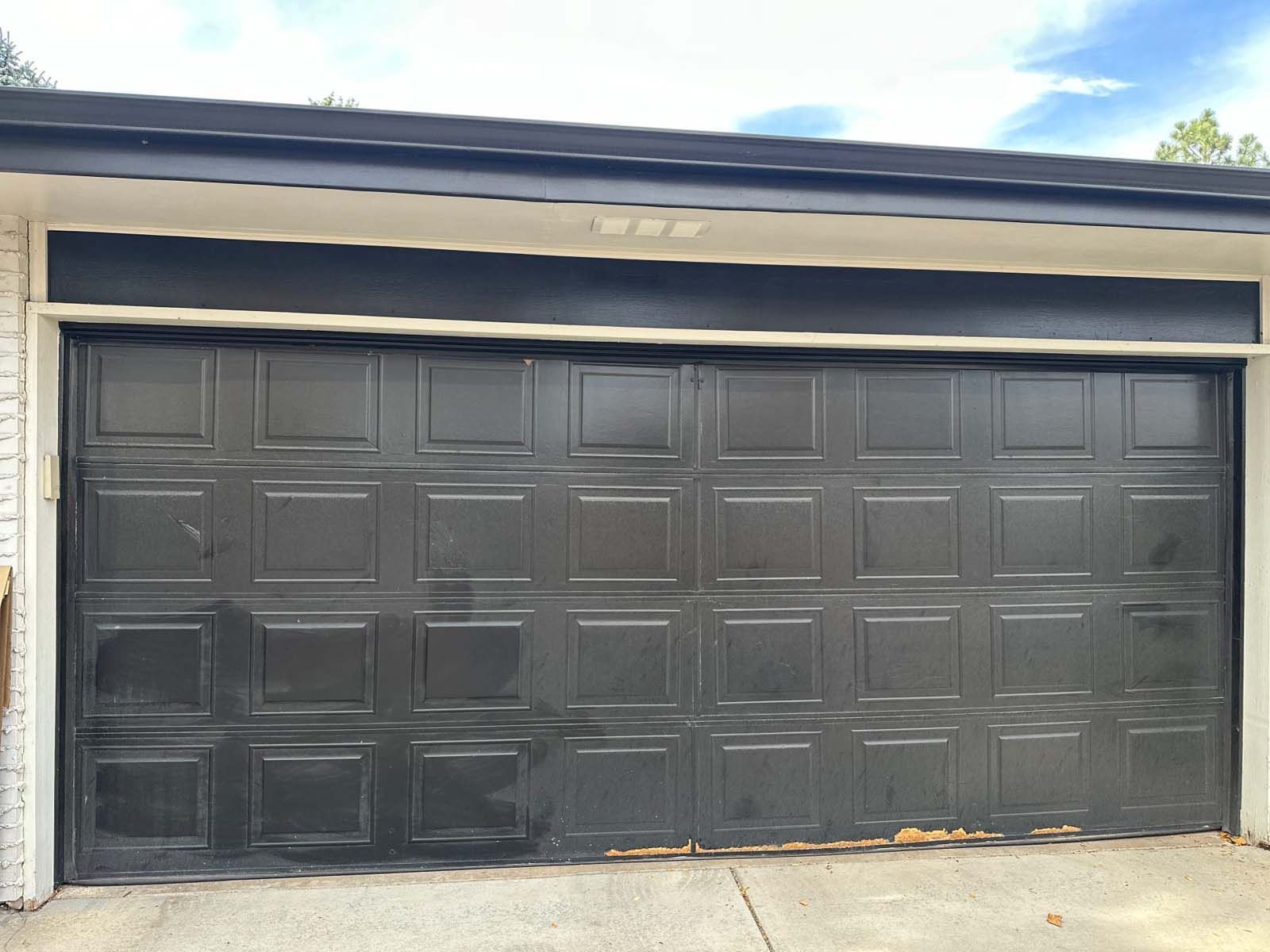 A black garage door is sitting on top of a white brick building.