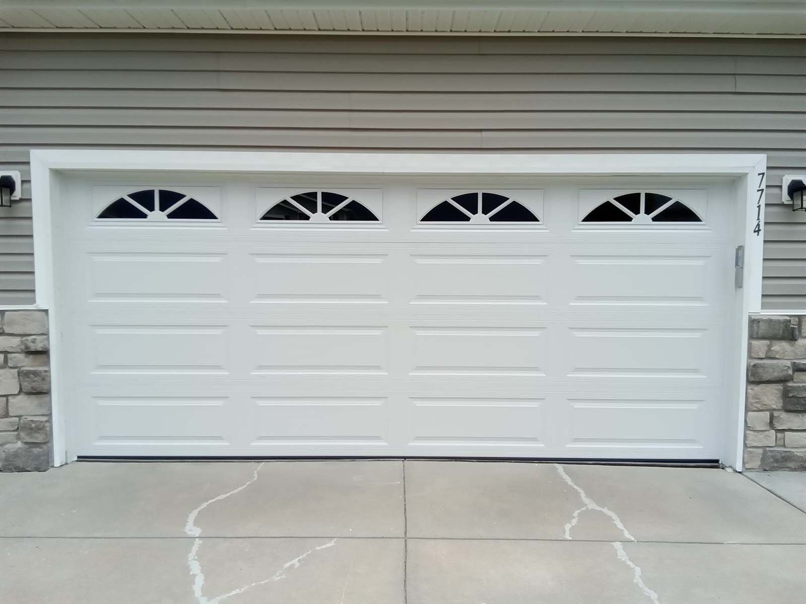 A white garage door with arched windows on the side of a house
