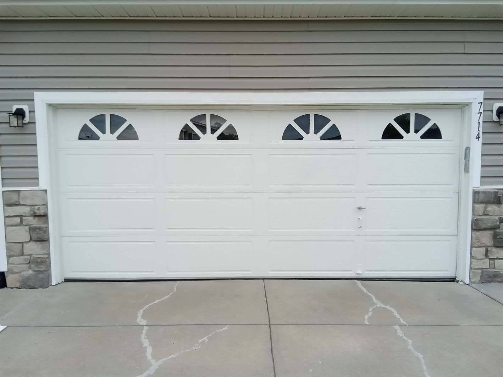 A white garage door with three windows on the side of a house.