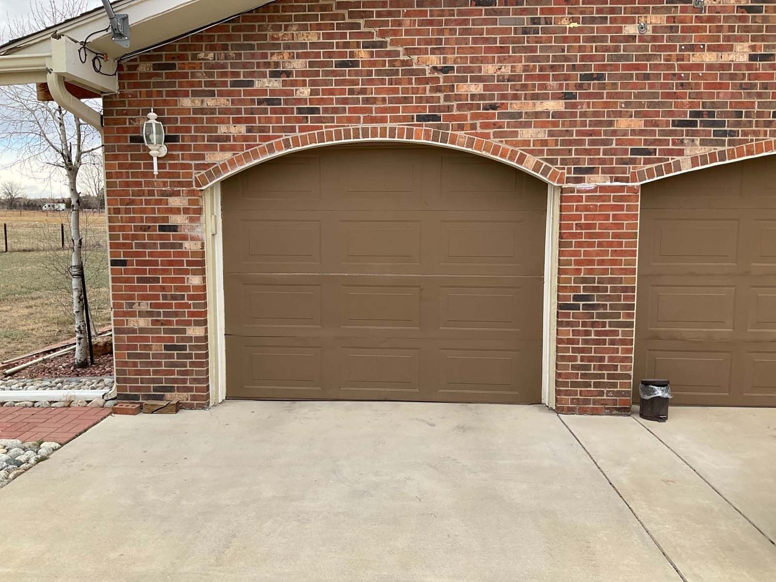 A brick building with two brown garage doors and a concrete driveway.