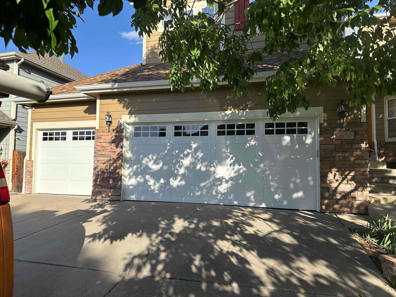A car is parked in front of a house with two garage doors.