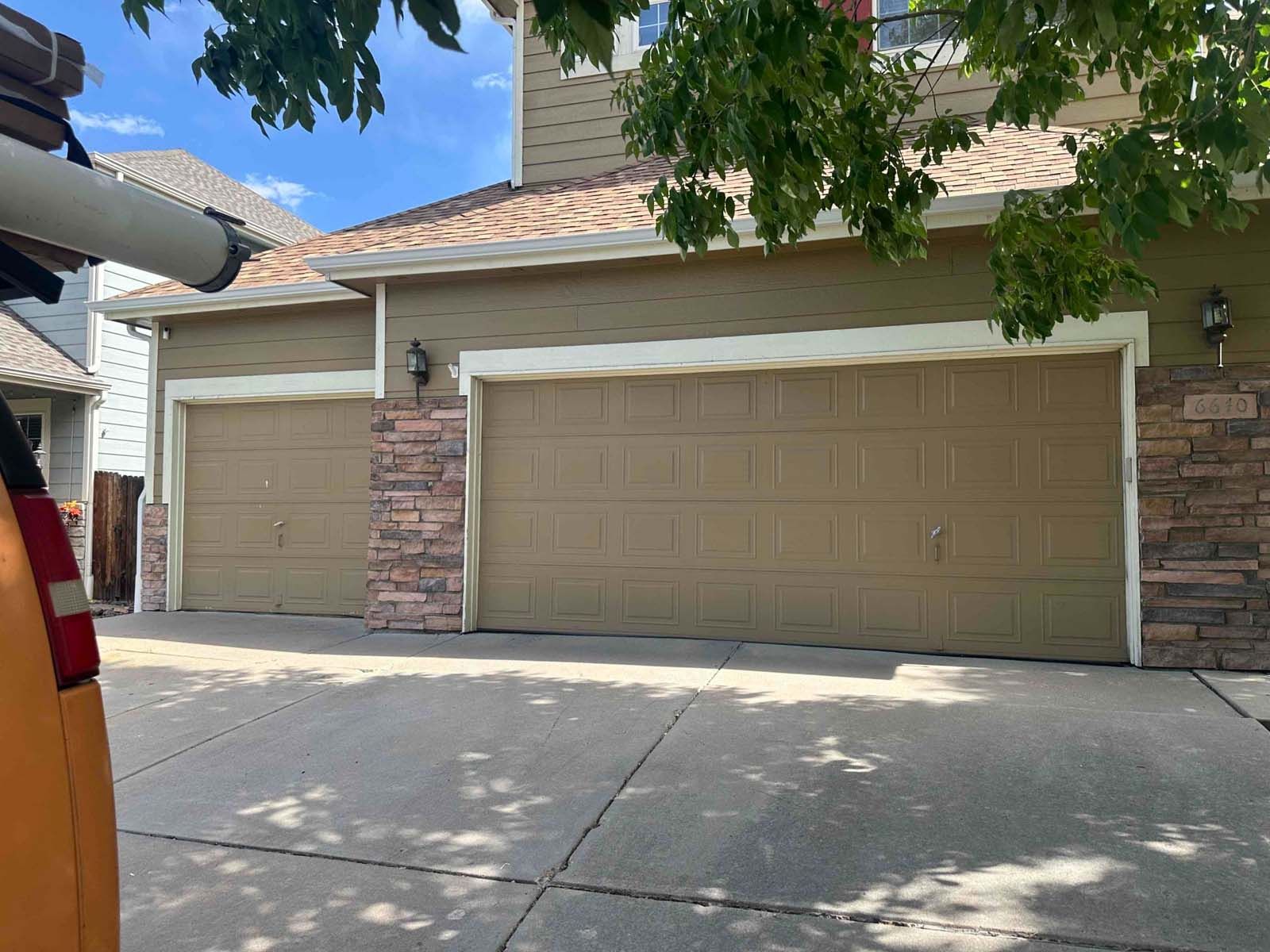 A car is parked in front of a house with three garage doors.