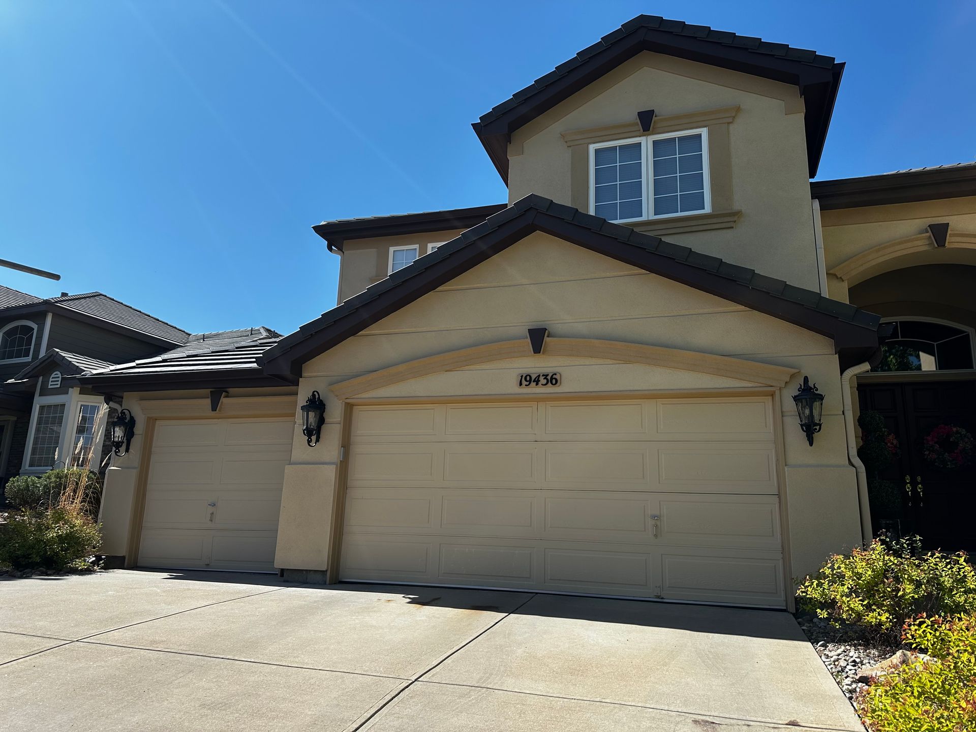 A large house with three garage doors and a blue sky in the background
