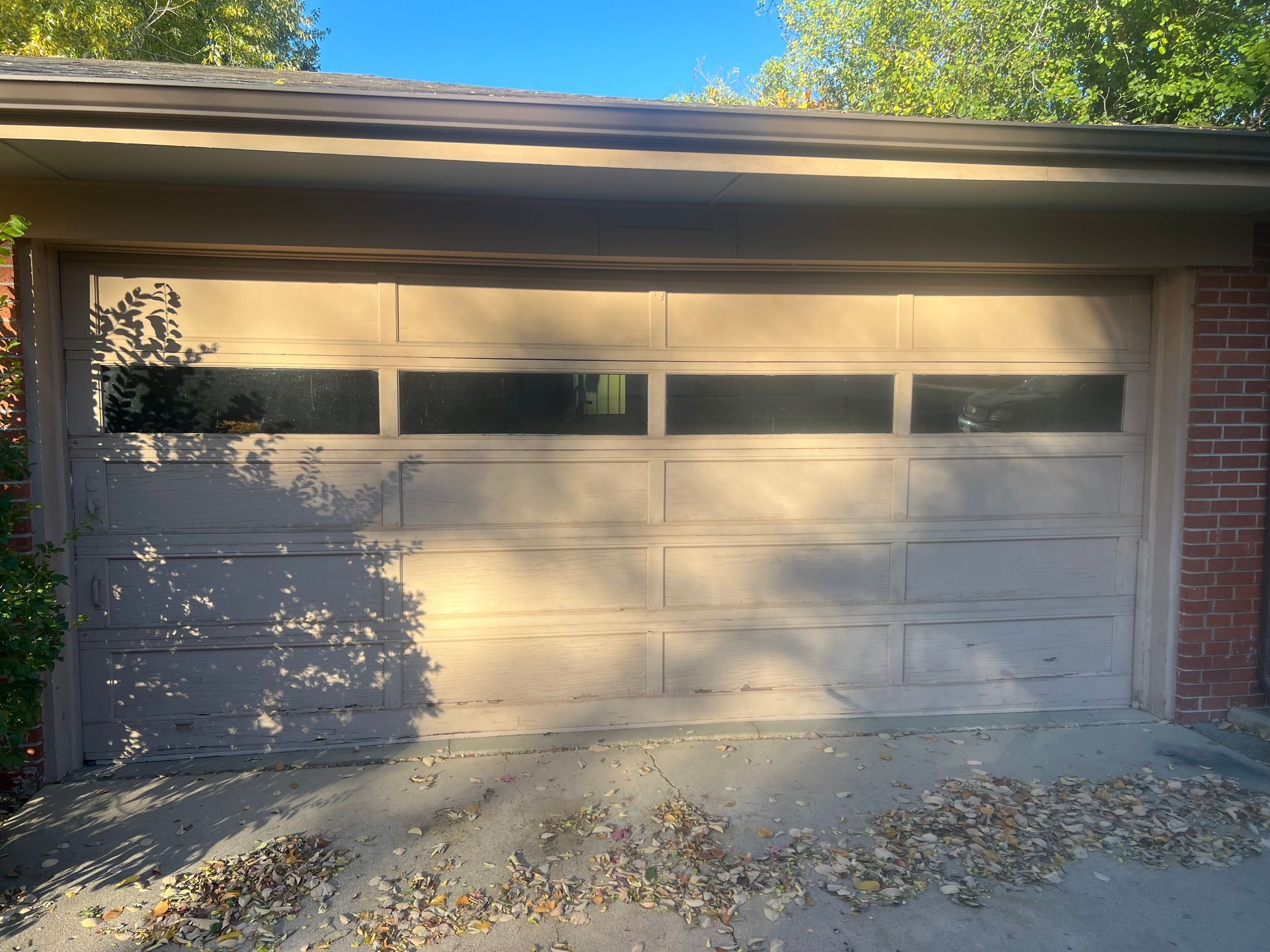 Tan garage door with windows, in shadow, against a brick building.