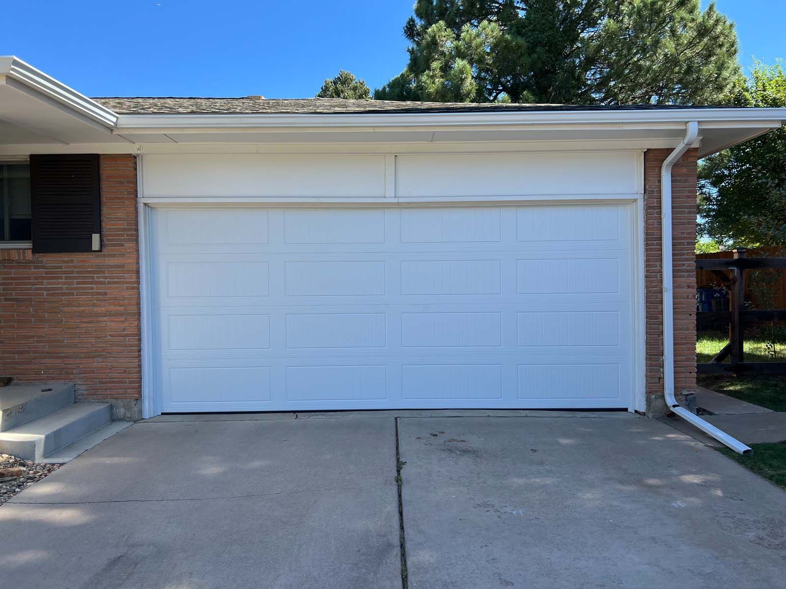 A white garage door is sitting in front of a brick house.