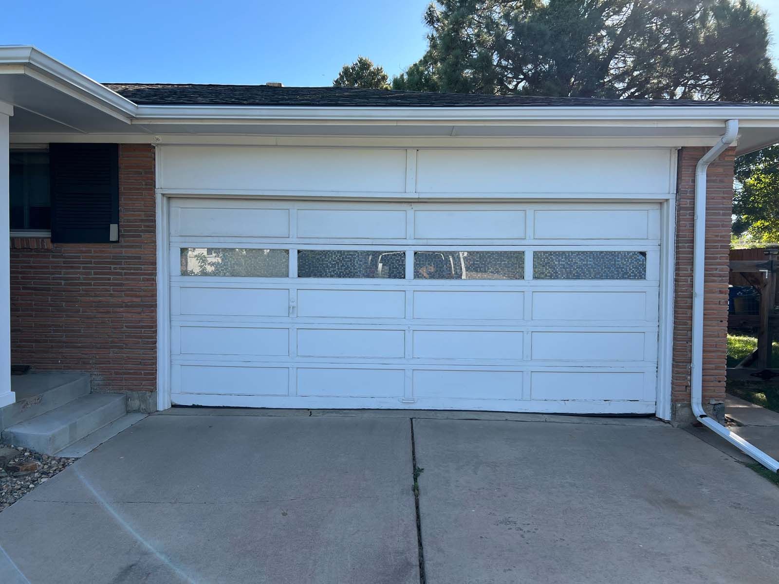 A white garage door is sitting in front of a brick house.