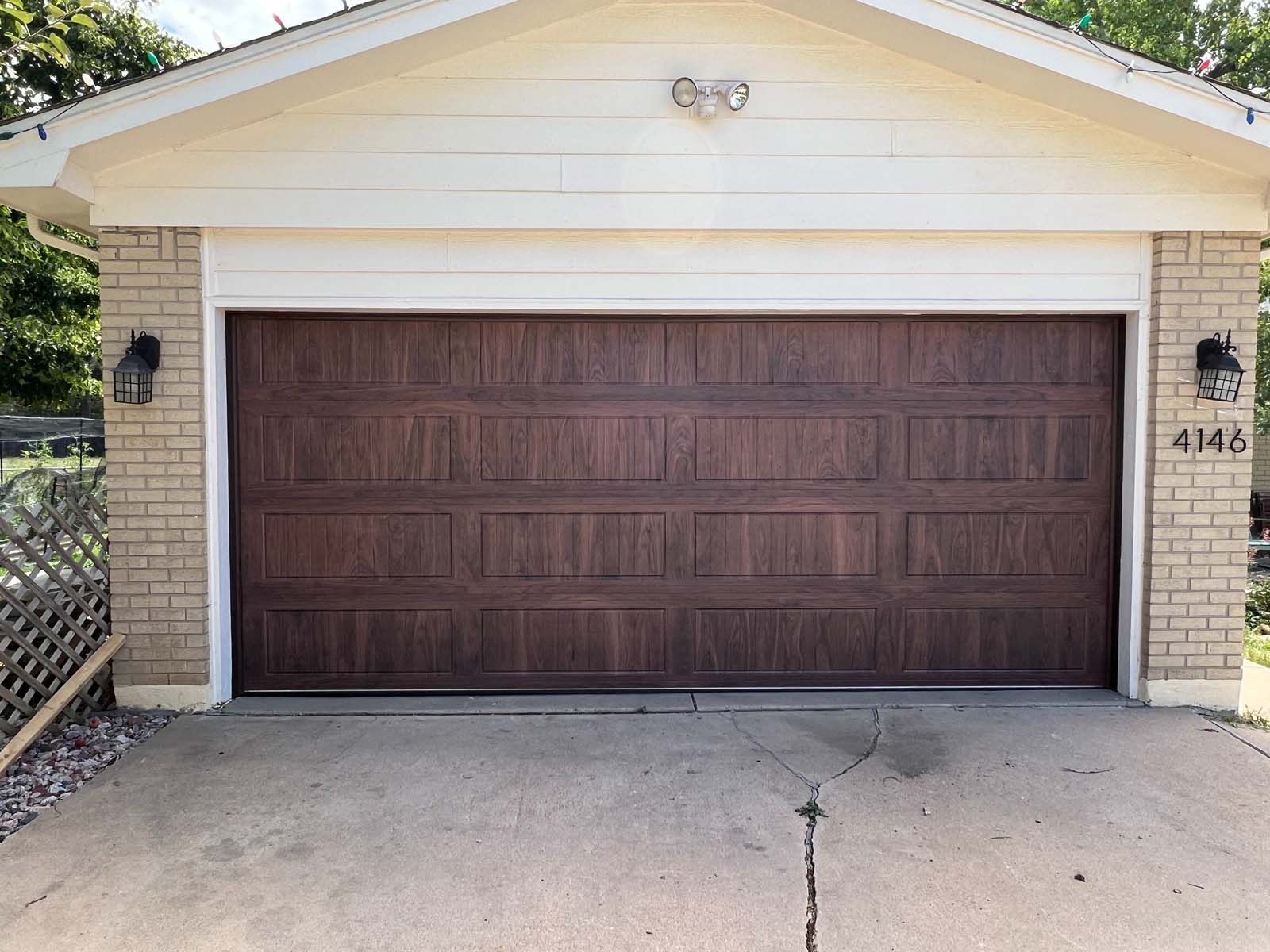 A wooden garage door is sitting in front of a brick house.