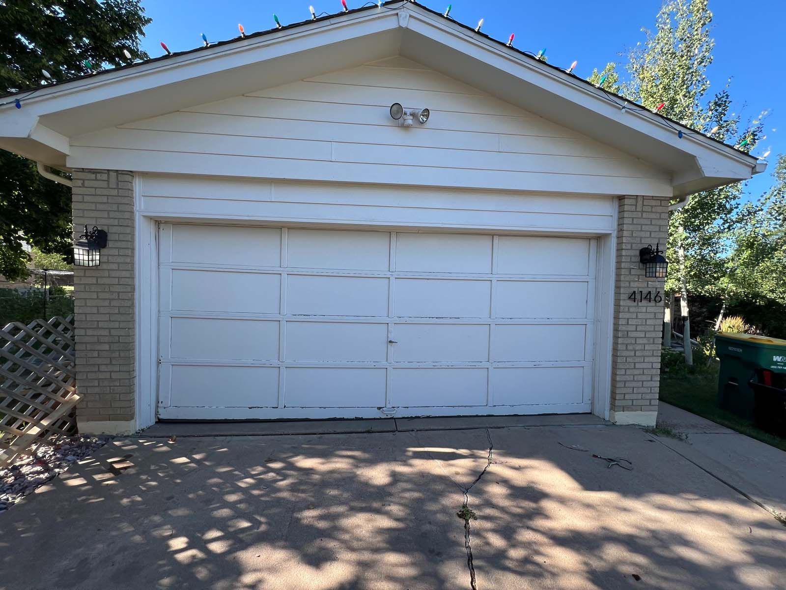 A white garage door is sitting in front of a brick house.