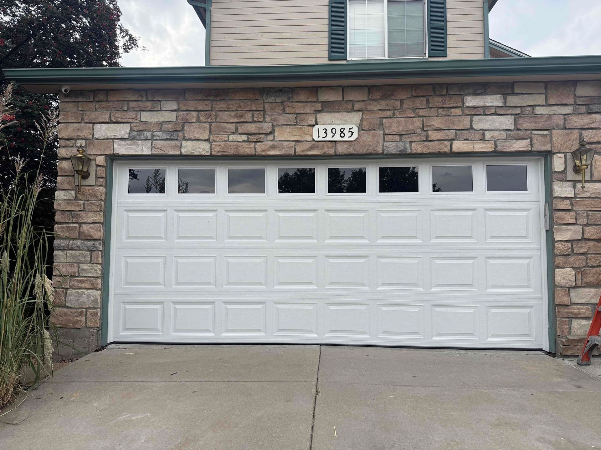 White garage door with windows, set in a stone facade, above a concrete driveway.