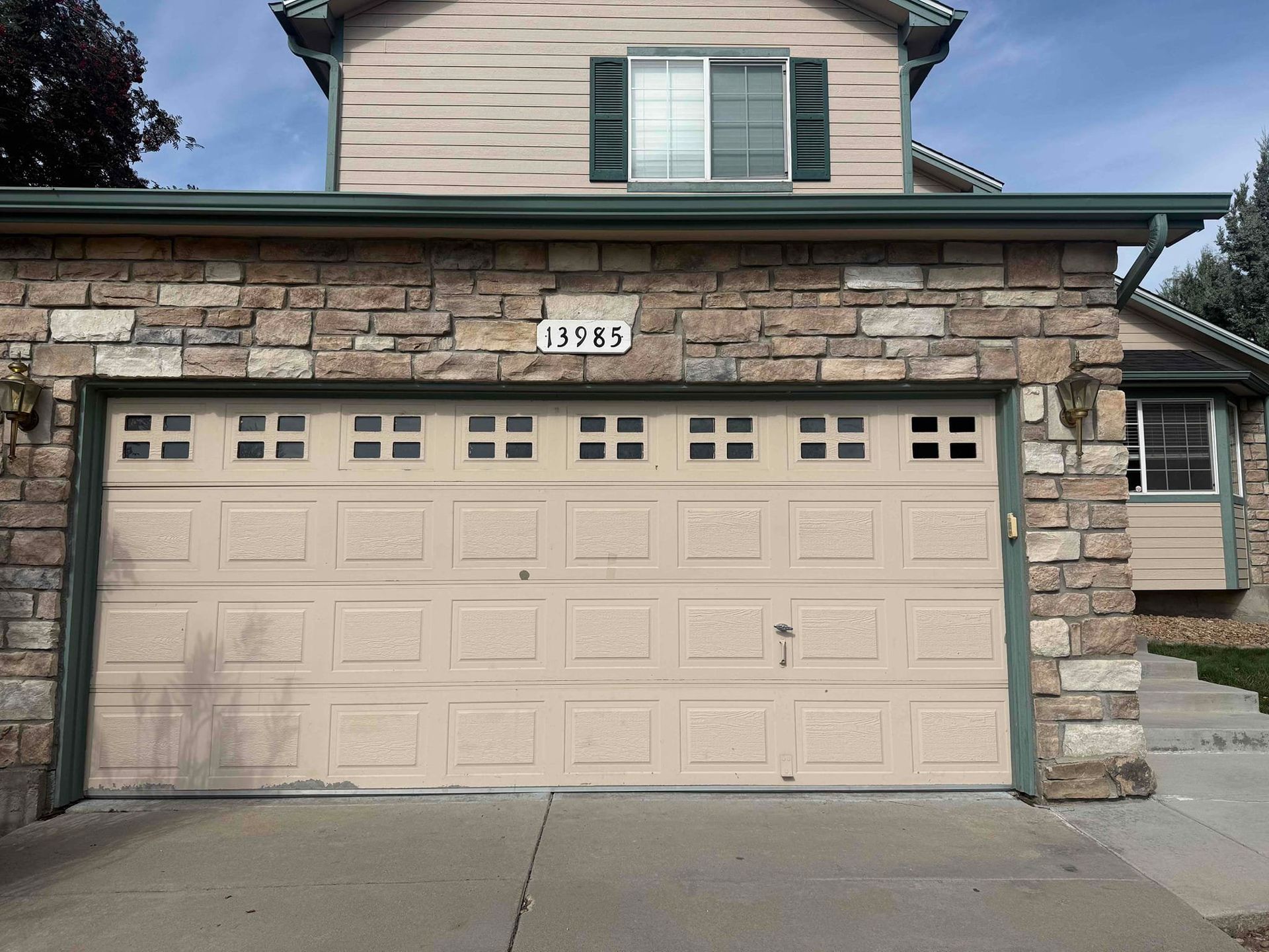 Garage door of a house with stone facade; beige door, green trim, address 15584 above door.