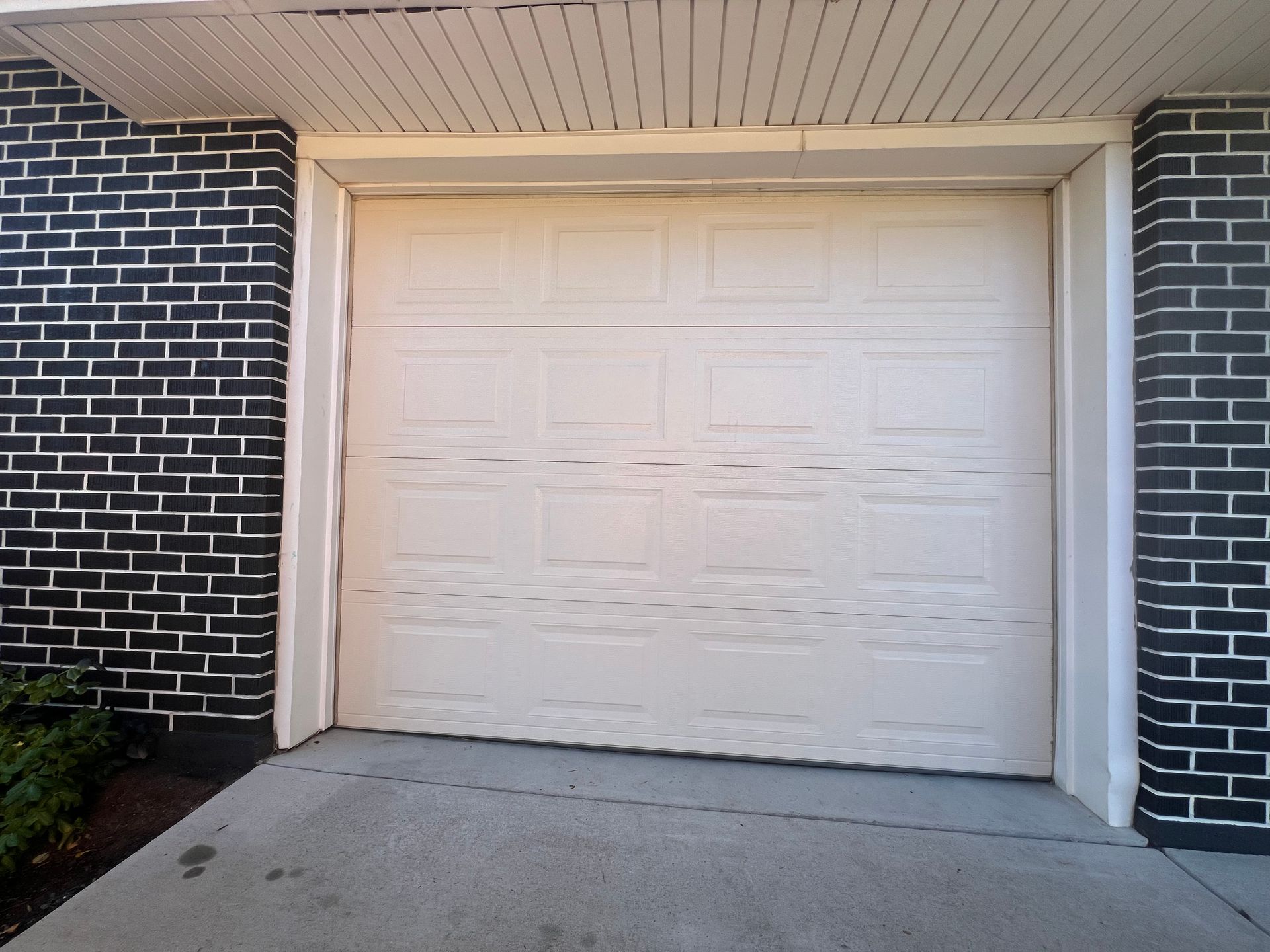 White garage door framed by white trim, flanked by black brick walls. Concrete driveway in front.