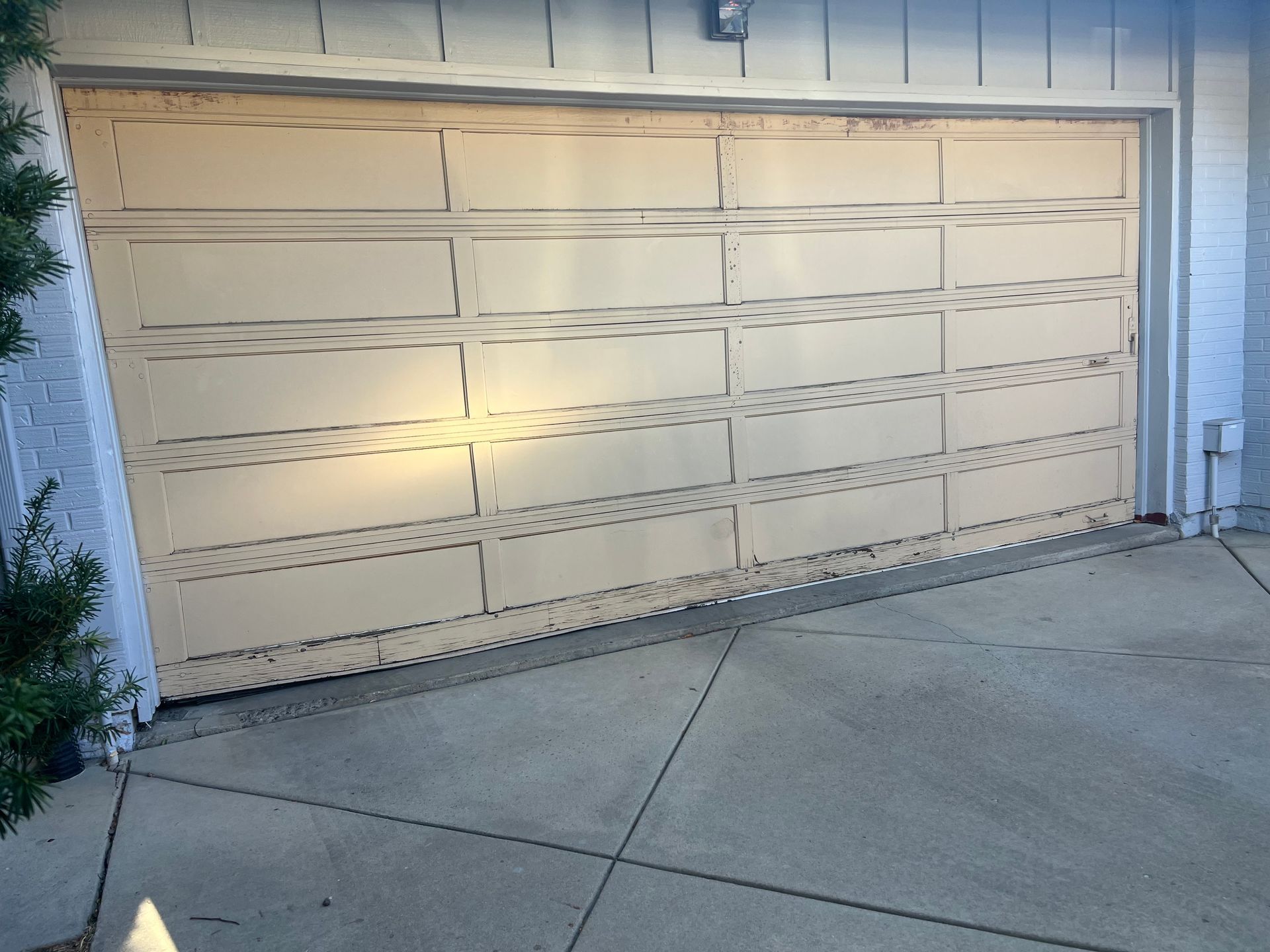 Beige garage door partially open, set in a concrete driveway.