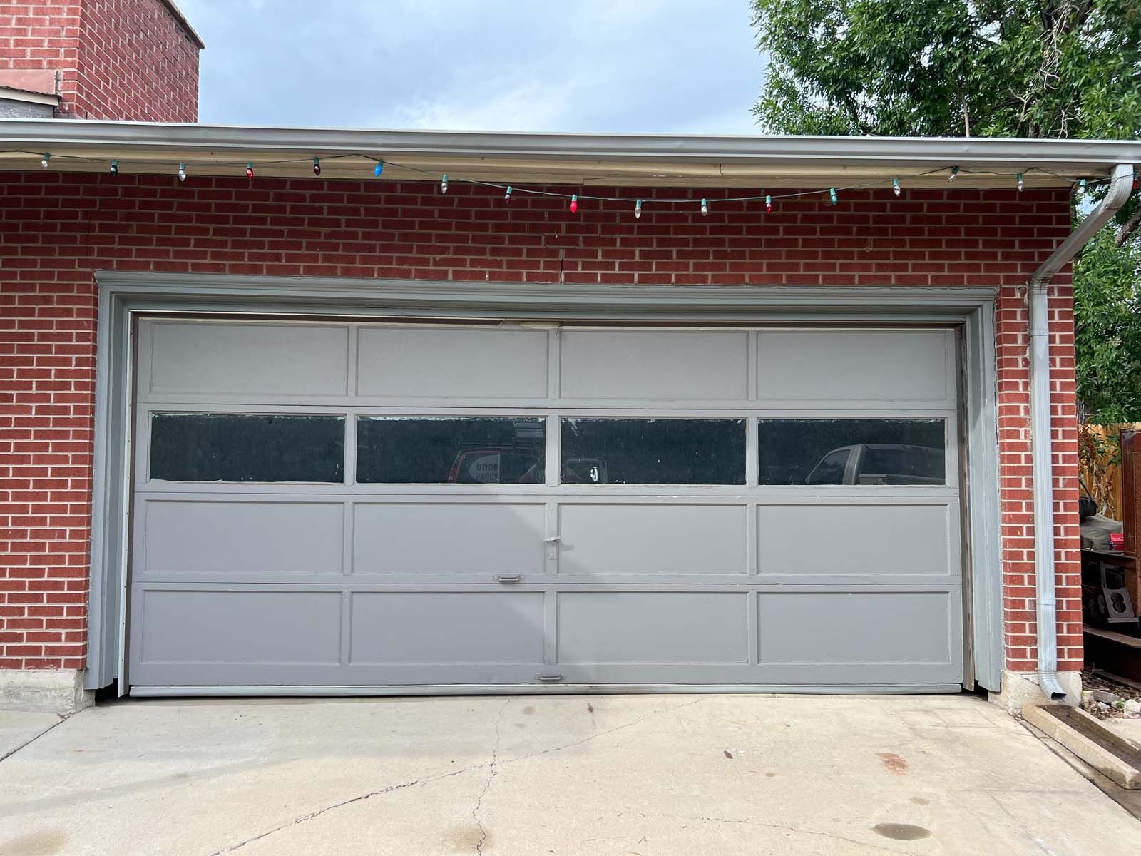 A gray garage door is sitting in front of a red brick building.