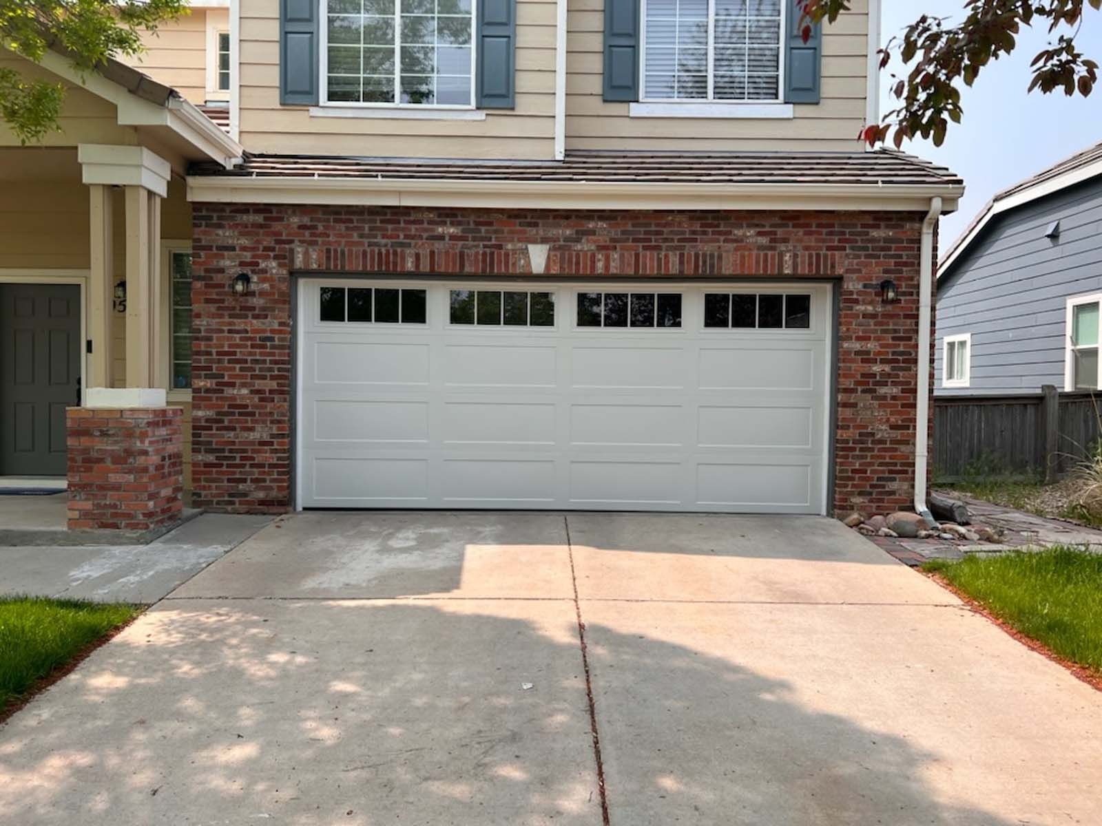 A white garage door is sitting in front of a brick house.