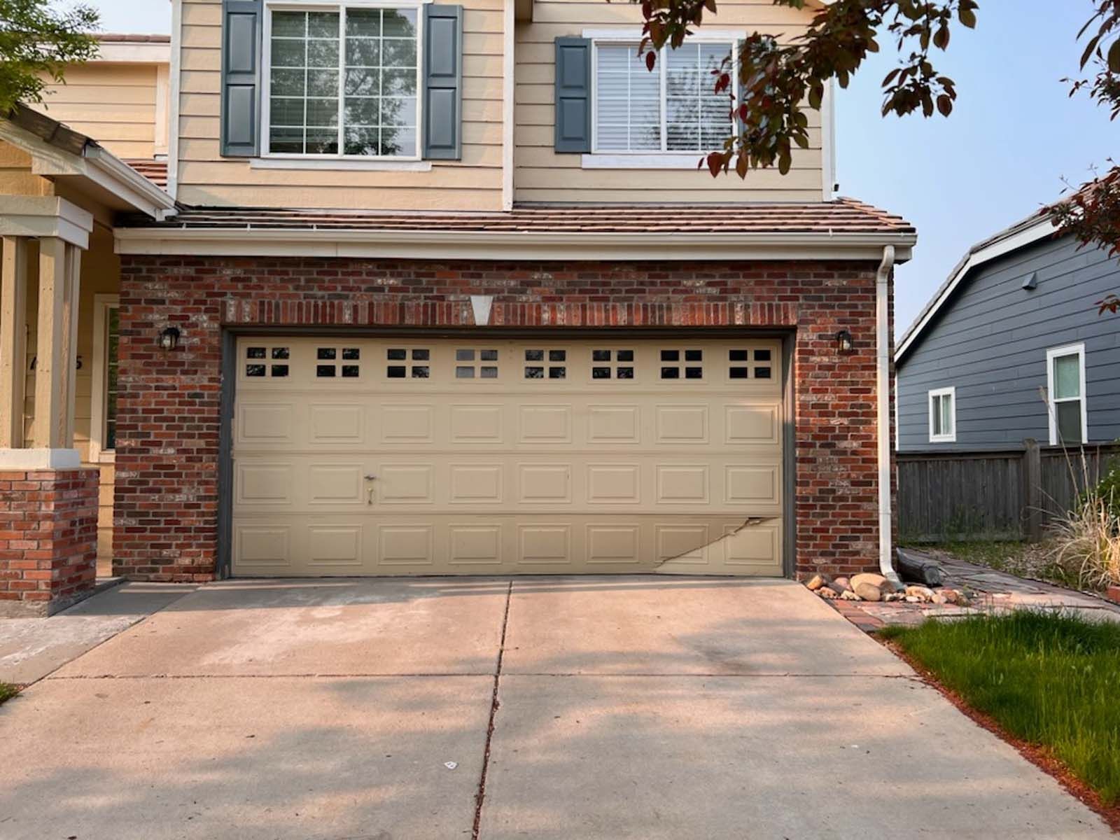 A house with a tan garage door and a brick wall.