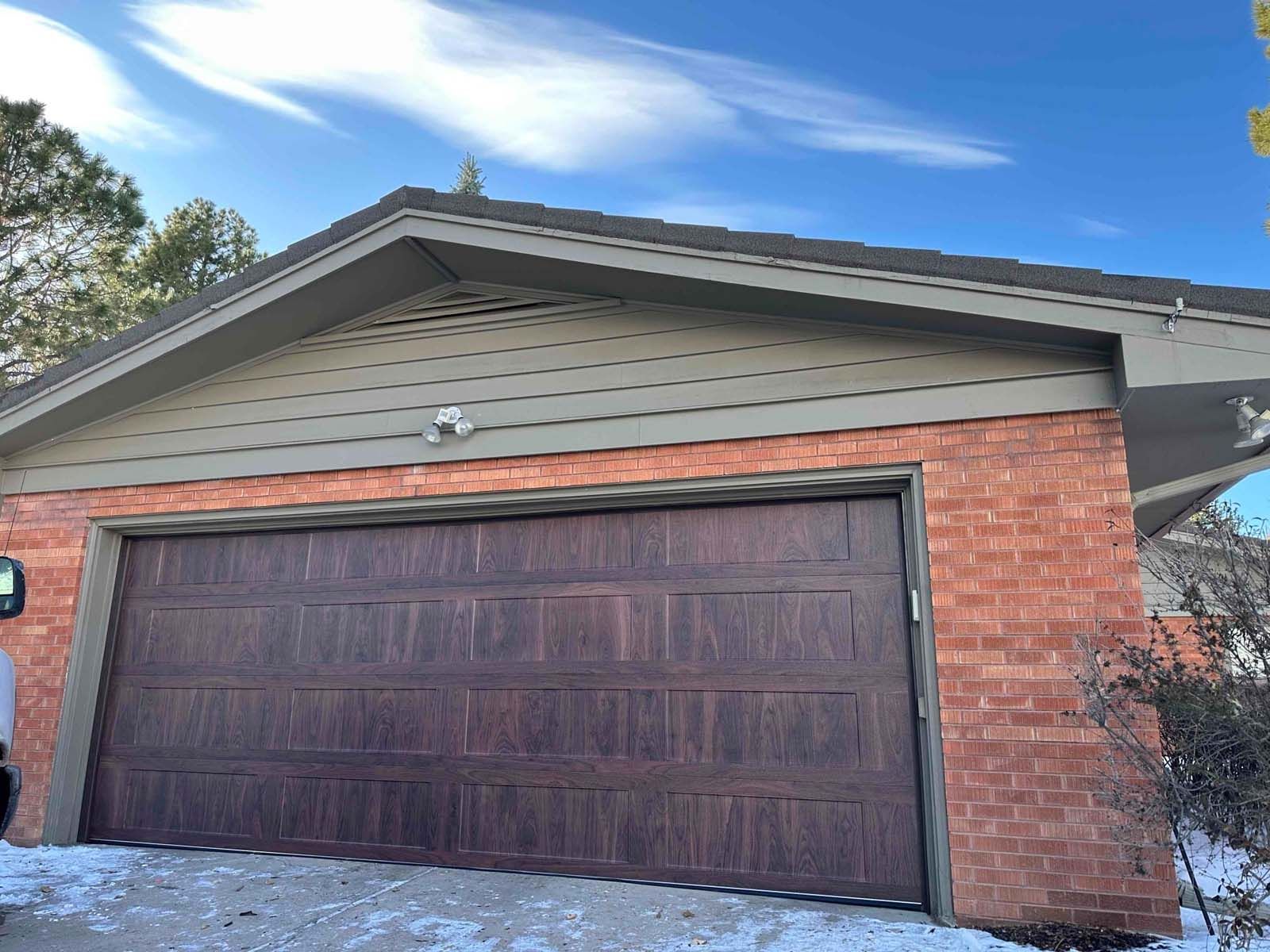 A man is standing in front of a garage door of a brick house.