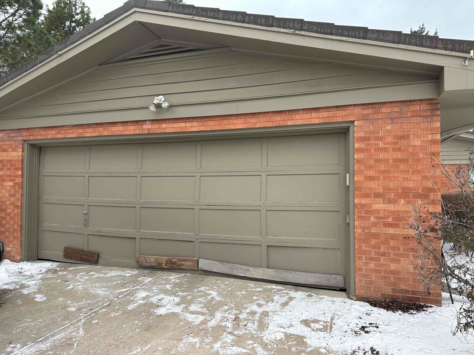 A brick house with a green garage door and snow on the ground.