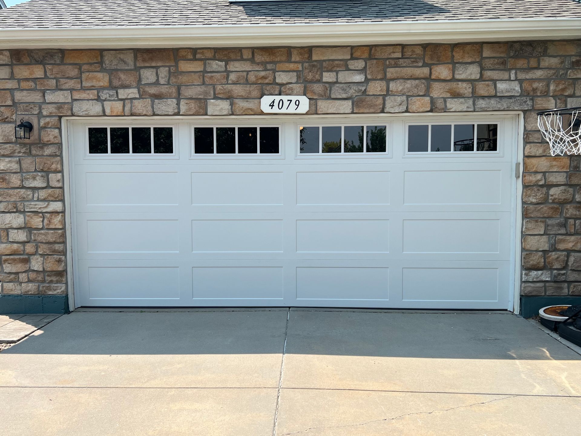 White garage door with windows, set in a stone wall, on a concrete driveway.