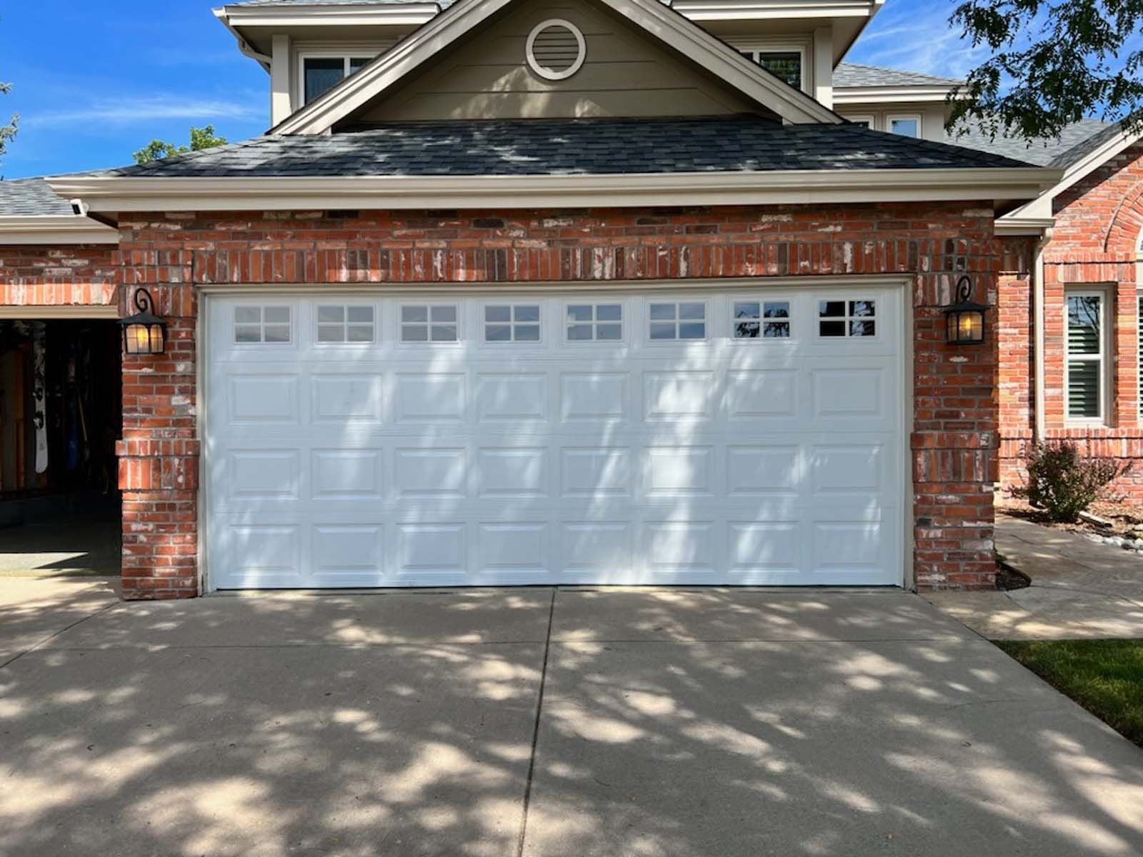 A white garage door is sitting in front of a brick house.