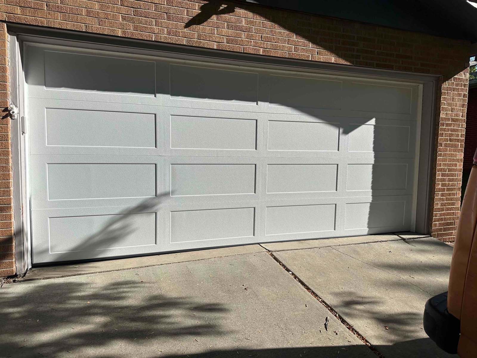 A white garage door is sitting in front of a brick building.