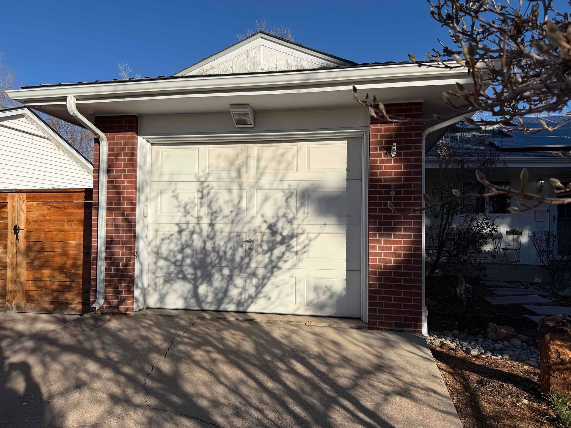 Brick garage with a white door, tree shadow, and a sunny sky.