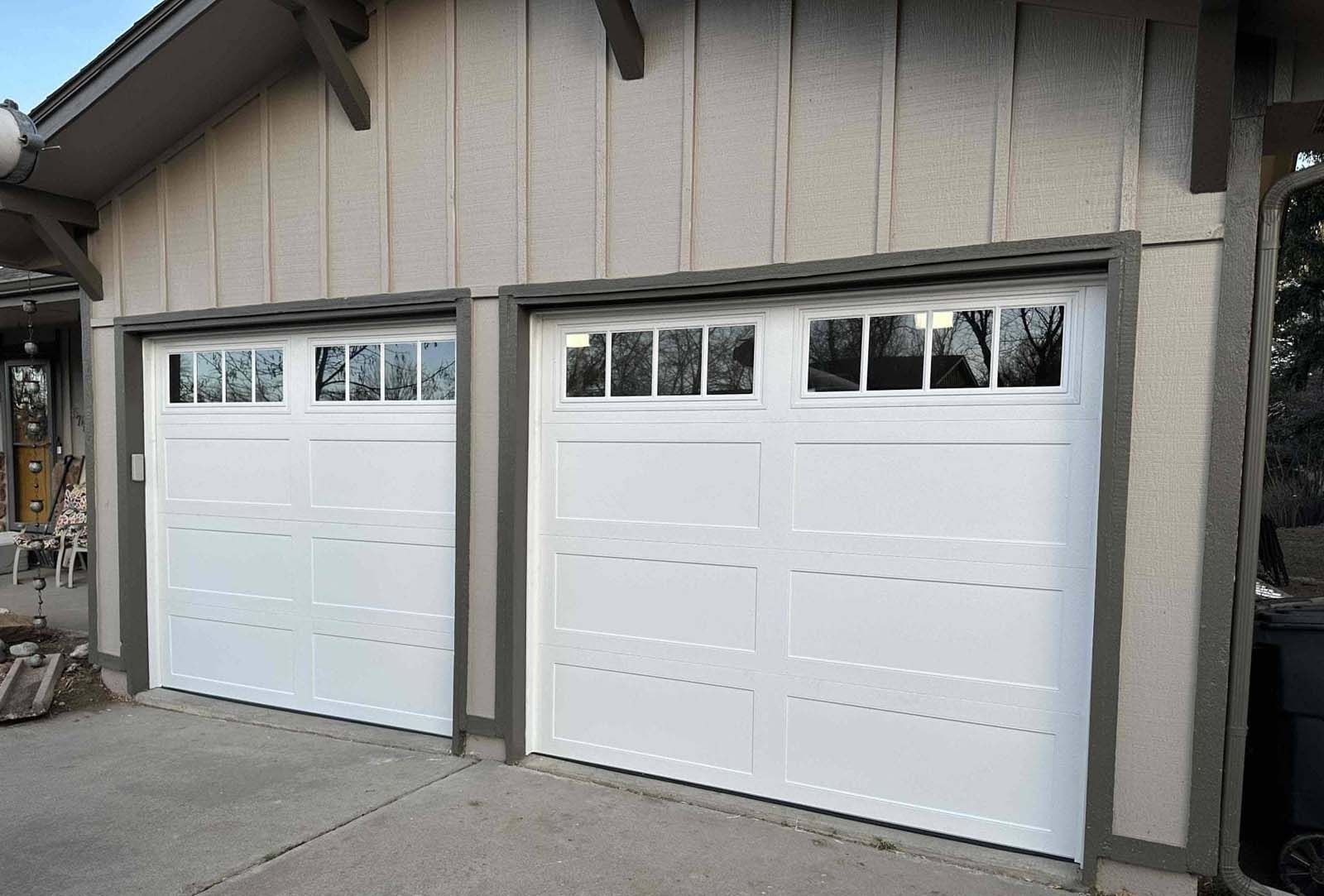 A pair of white garage doors are sitting next to each other on the side of a house.