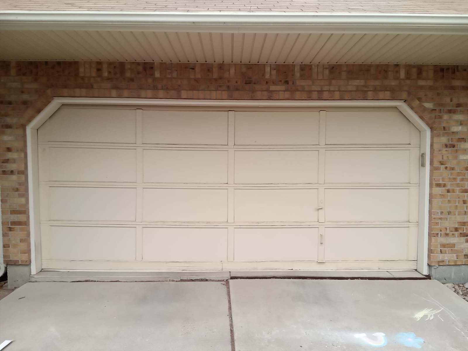 A white garage door with a brick wall behind it
