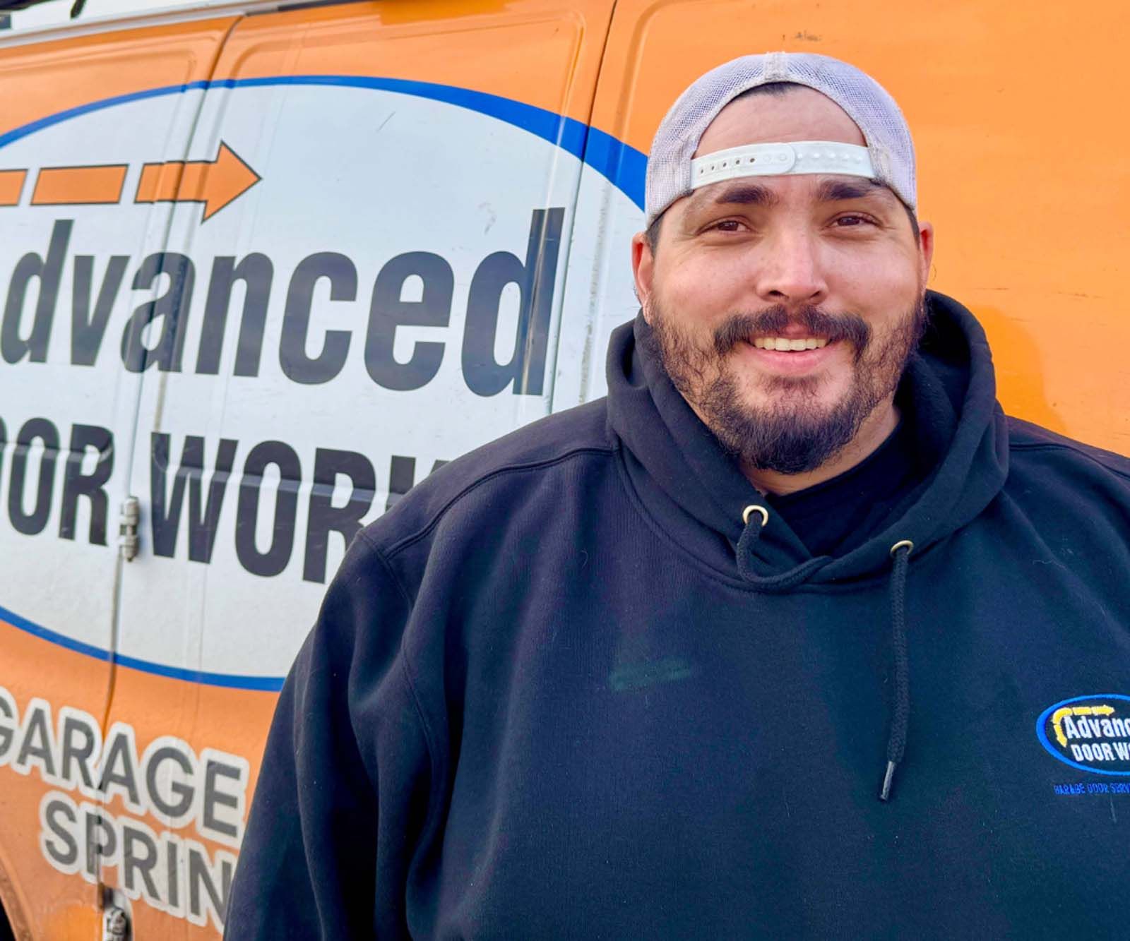 A man is standing in front of an orange van that says advanced for work