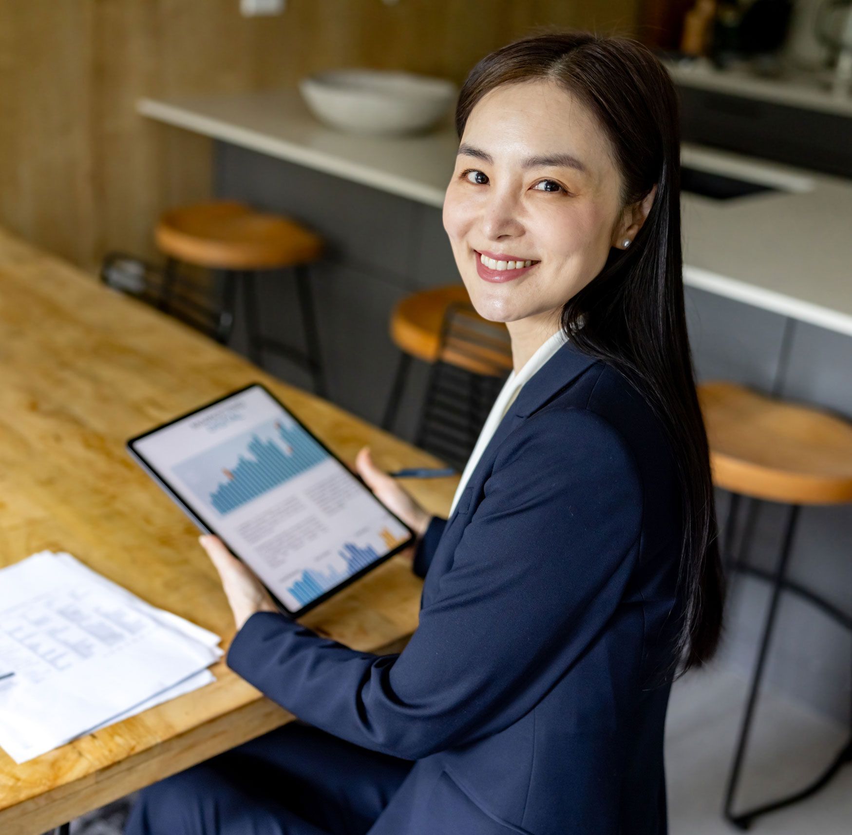 A woman in a suit is sitting at a table holding a tablet