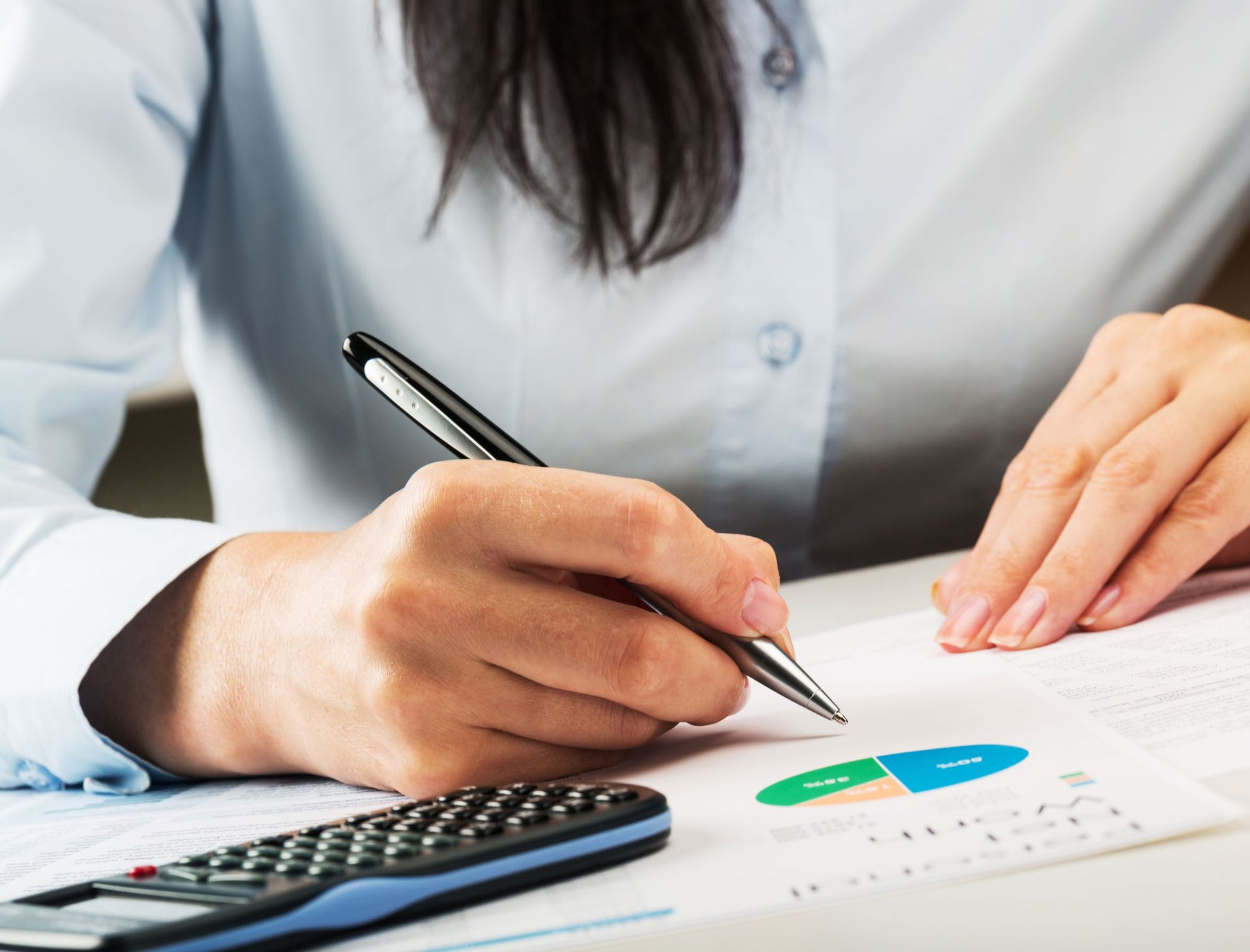 A woman is writing on a piece of paper next to a calculator.