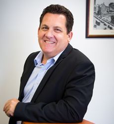 A man in a suit is sitting at a table and smiling.